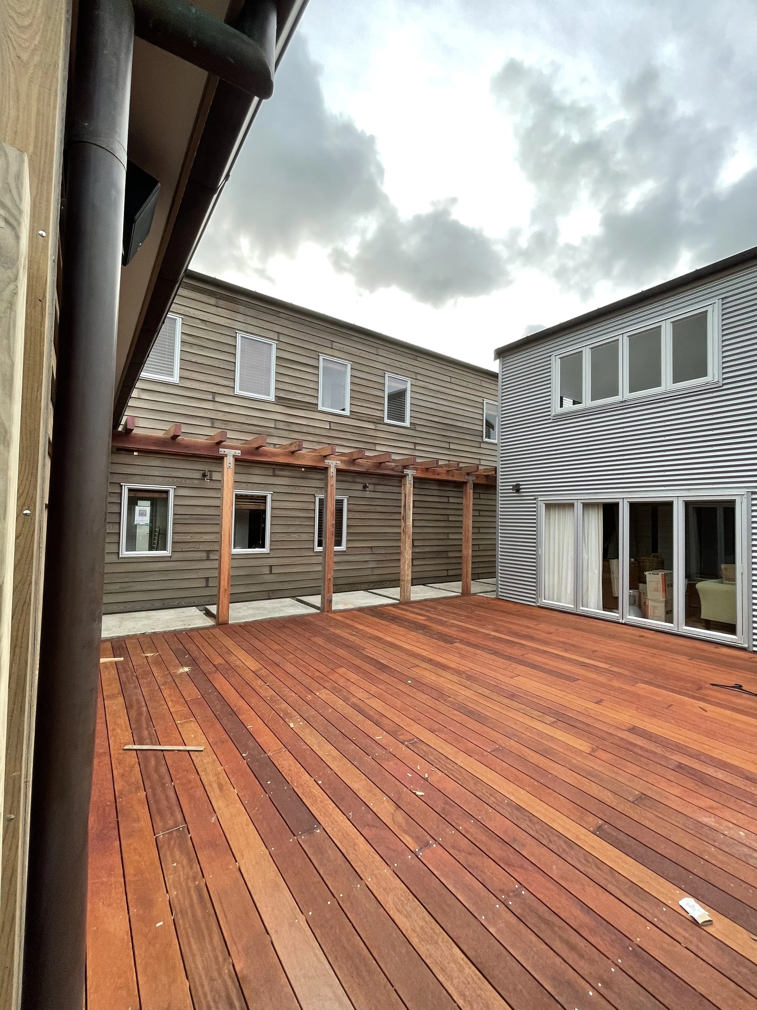 View of an outdoor wooden deck area with neighboring houses in the background and a cloudy sky.