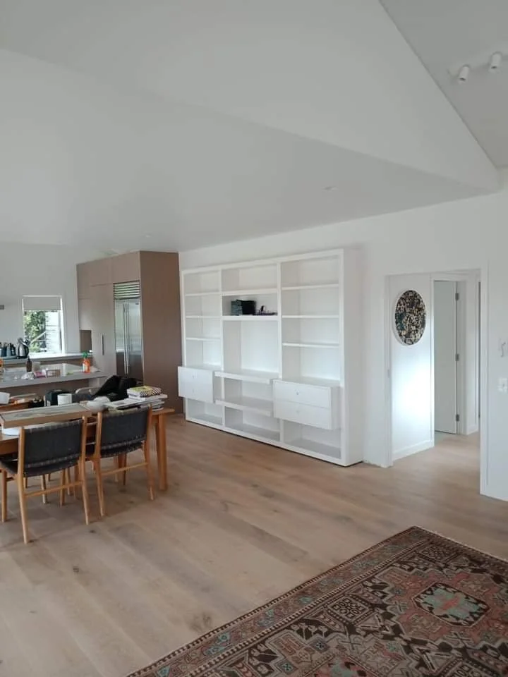 Open-concept living space with a dining area, kitchen, and built-in white shelving unit. Hardwood floors and a decorative area rug are visible.