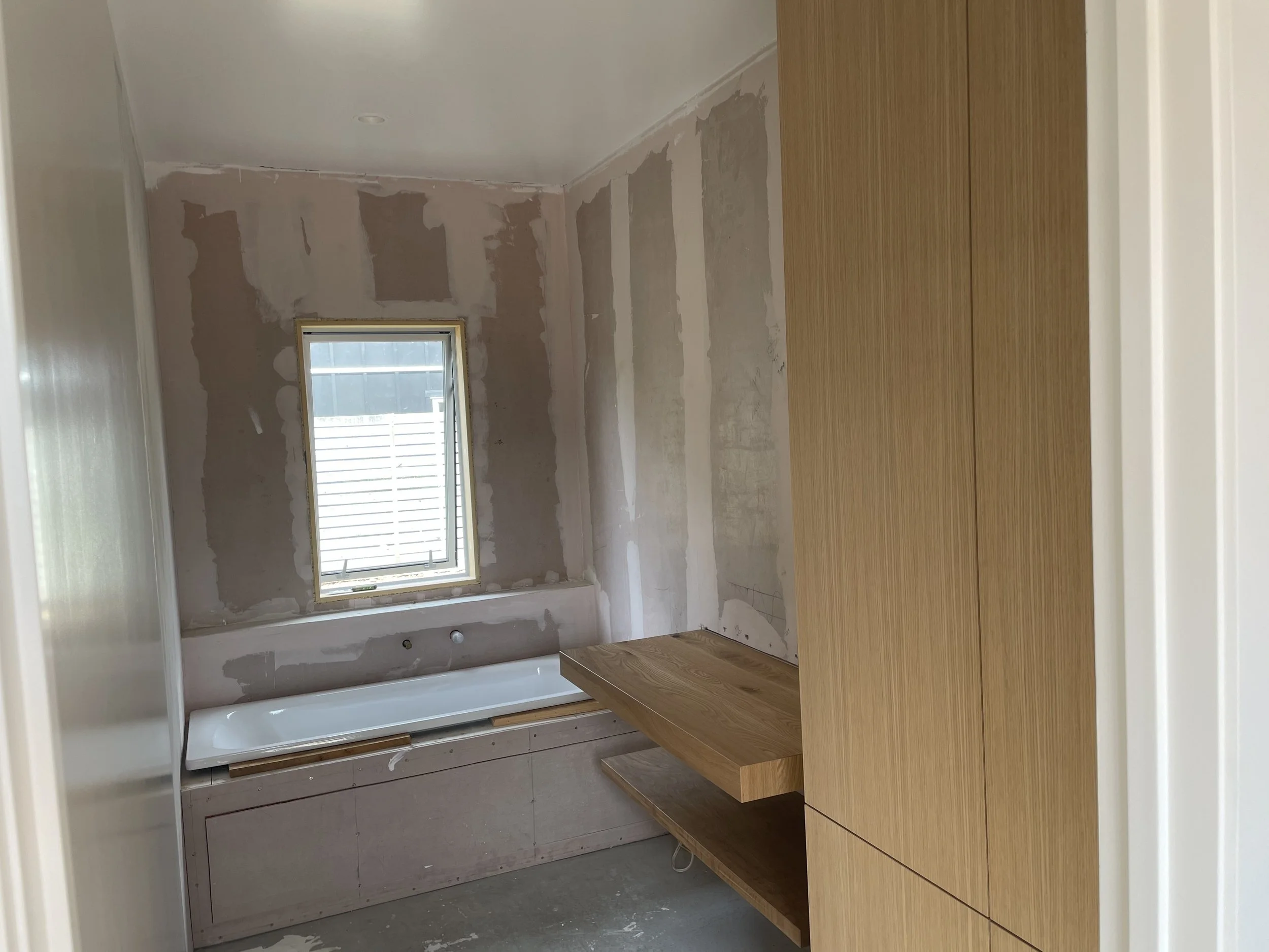 Room under renovation with unfinished walls, window, a built-in bathtub, and wooden cabinetry.