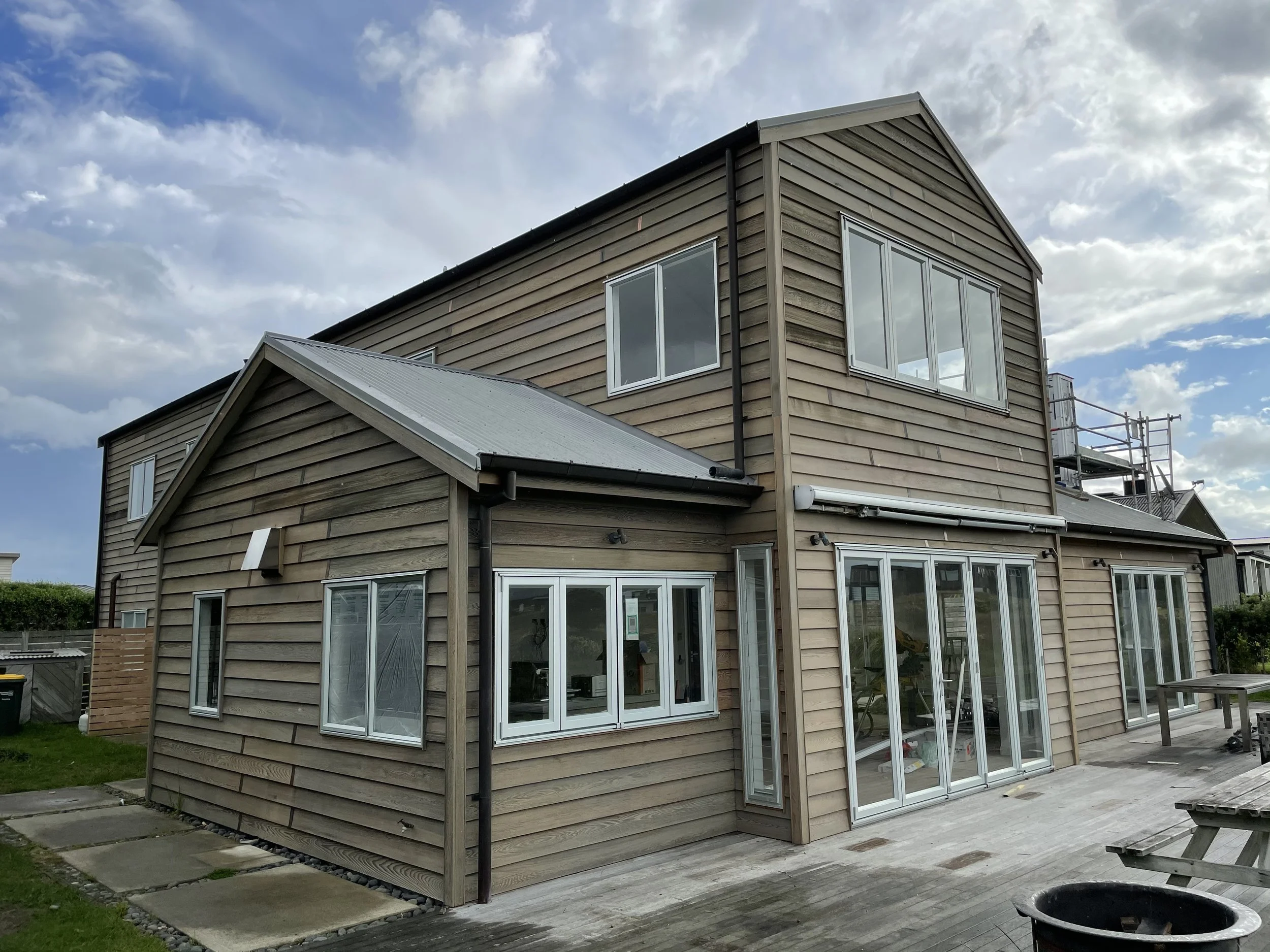 A modern house with wooden siding, large windows, and a metal roof under a partly cloudy sky.