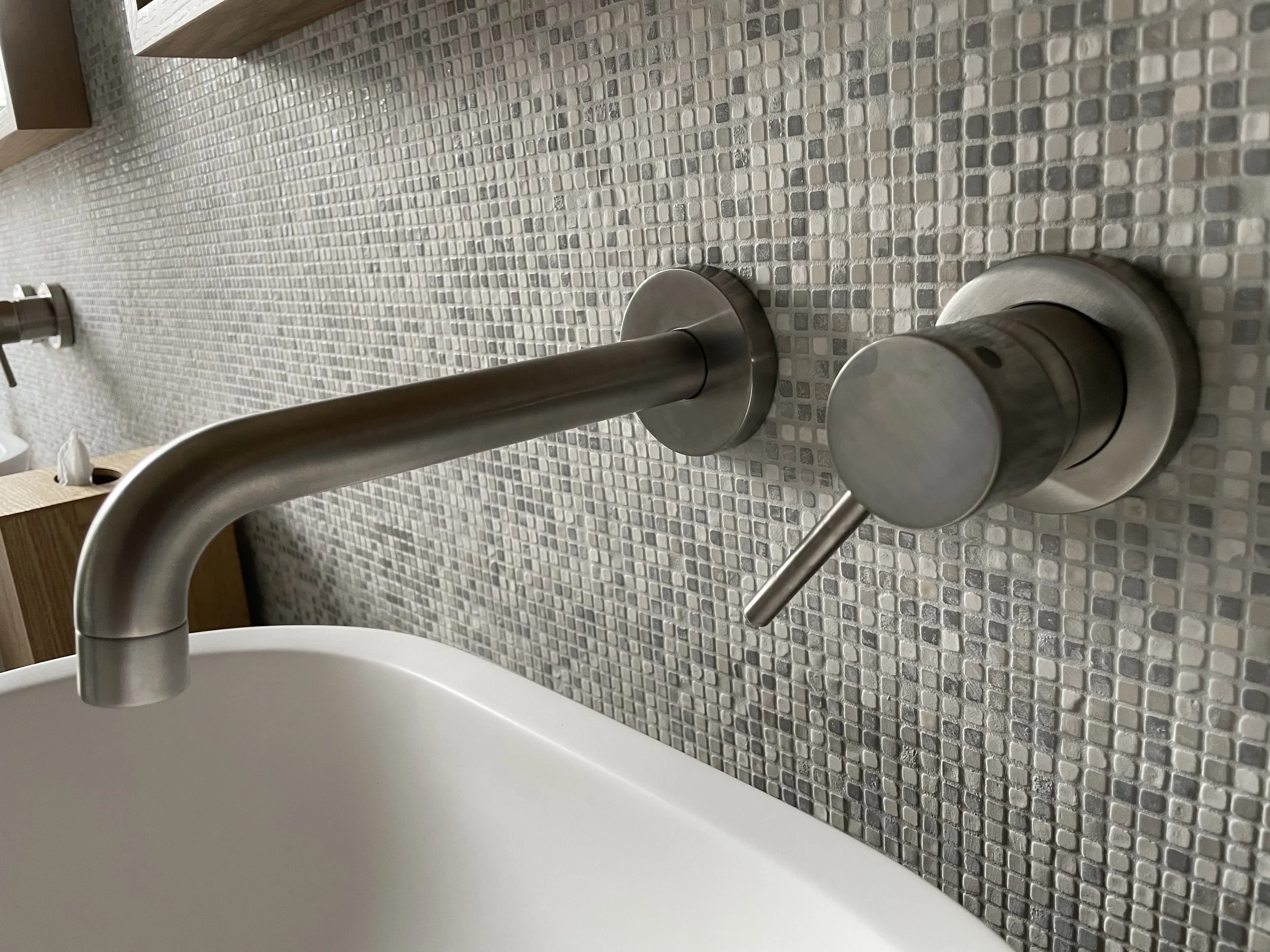 Close-up of a modern stainless steel faucet on a kitchen countertop with small square gray and beige mosaic tiles in the background.