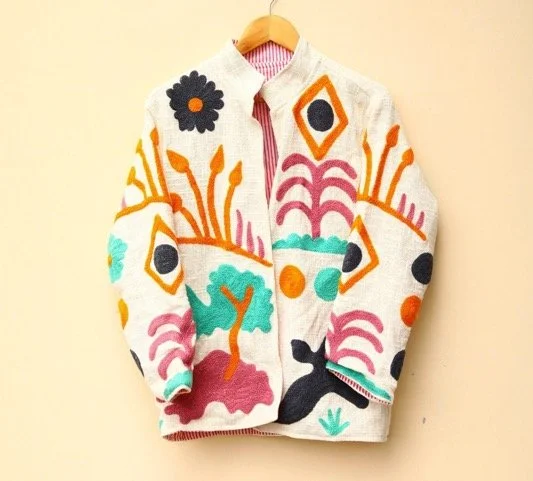 Colorful embroidered sweater hanging on a wooden hanger against a beige wall.