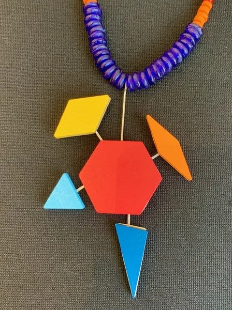 Colorful geometric necklace with yellow, orange, blue, red shapes on black background. Created by Theresa Killgore.