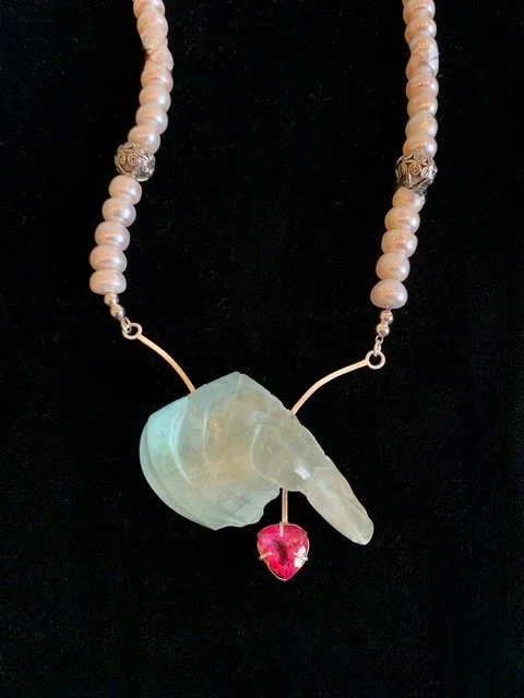 Necklace with pearl beads, a carved light green stone pendant, and a pink gemstone accent on a black background.