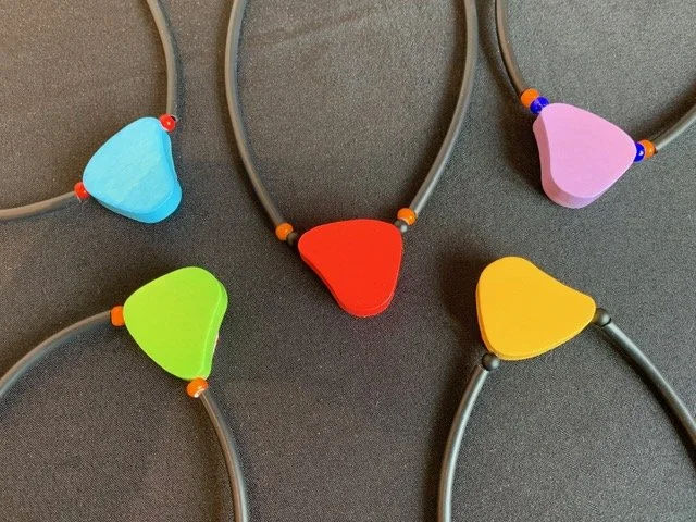 Colorful plastic necklaces with triangular pendants in blue, purple, green, red, yellow, and pink on a black background.