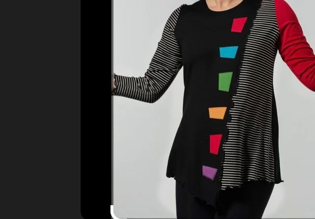 A woman wearing a black and red long sleeve shirt with colorful geometric shapes on the front, standing against a plain background.