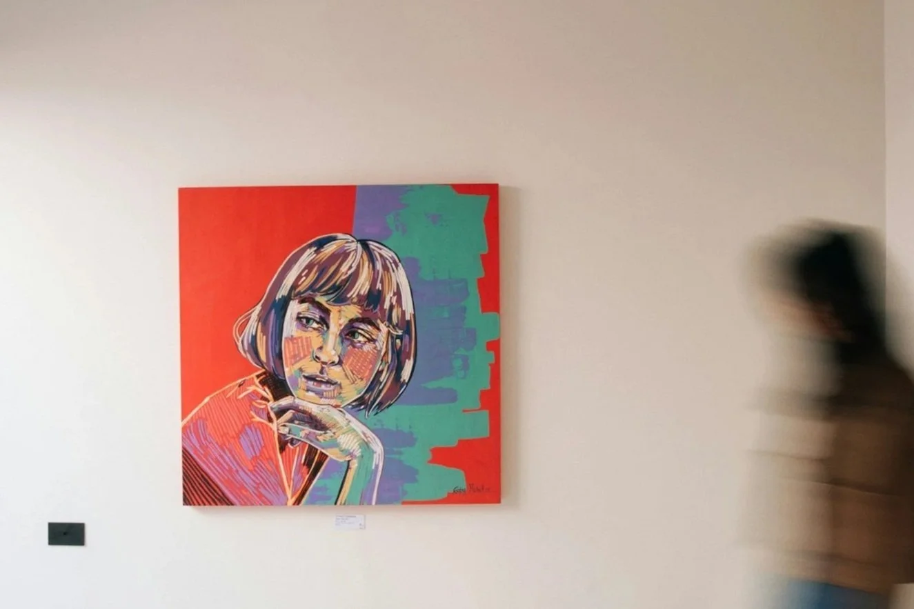 Colorful portrait of a woman with a bob haircut, resting her chin on her hand in an art gallery.