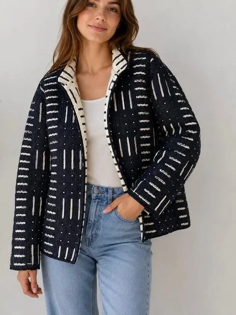 Woman with long brown hair wearing a navy and white patterned jacket over a white top and light blue jeans, posing against a plain background.
