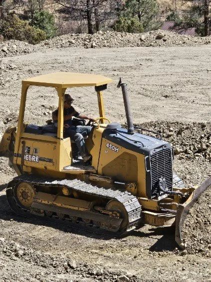 Small yellow bulldozer working on a dirt construction site with a person operating it.
