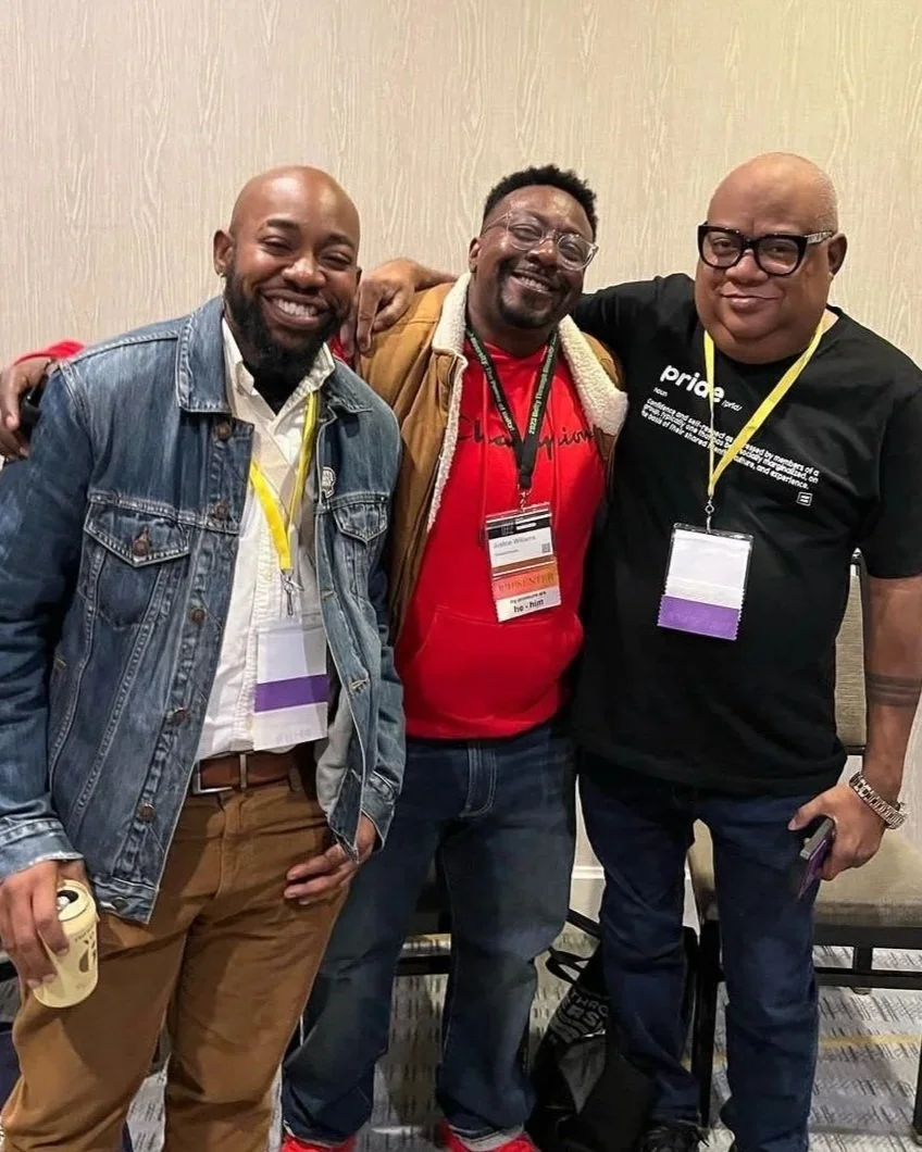 Three men smiling and standing with their arms around each other at a conference. They are wearing conference badges around their necks.