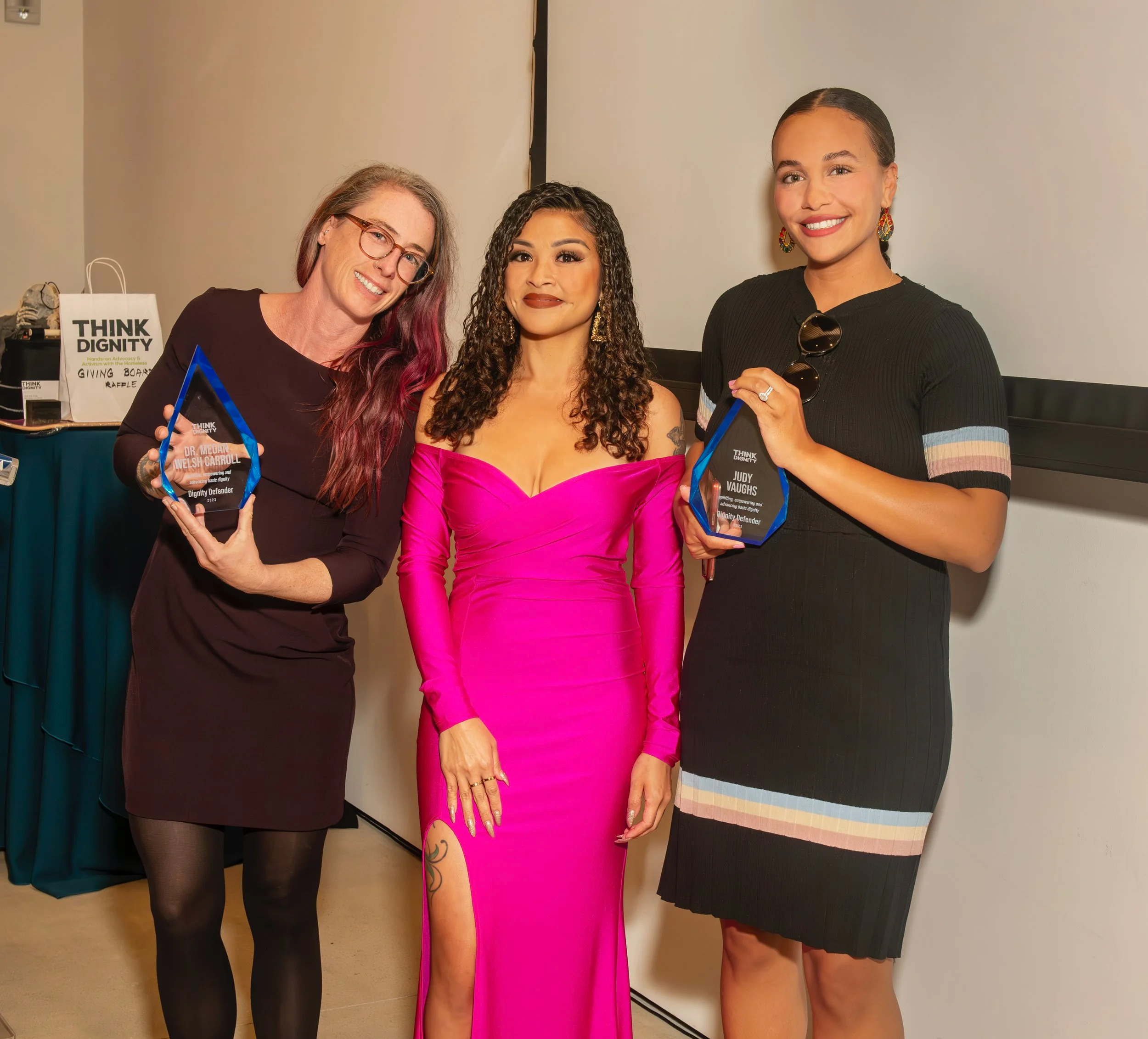 Three women posing together, two holding awards, at an indoor event.