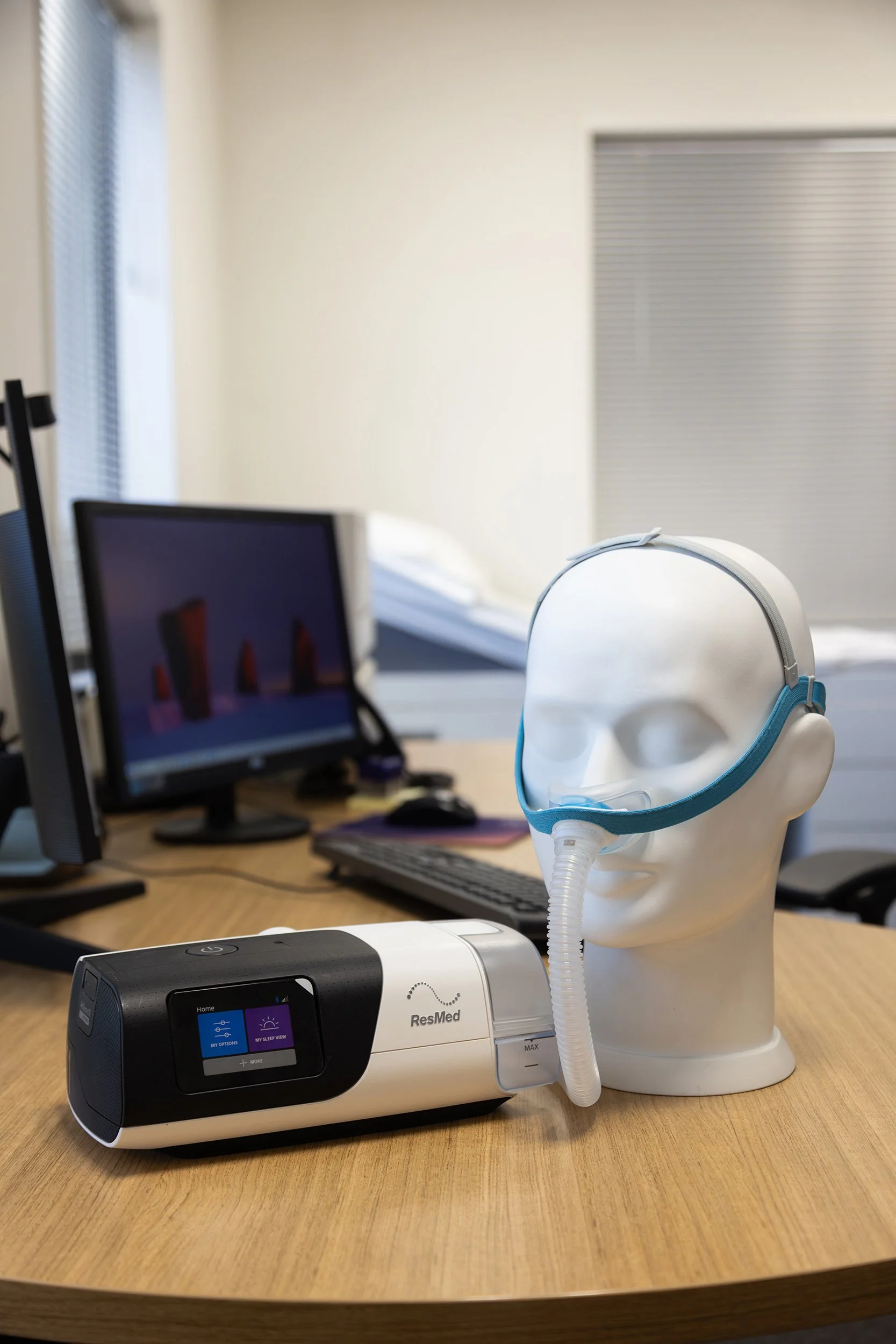 Sleep Medical equipment, including a medical CPAP machine on a wooden table with a mannequin head wearing a CPAP mask connected to the machine.