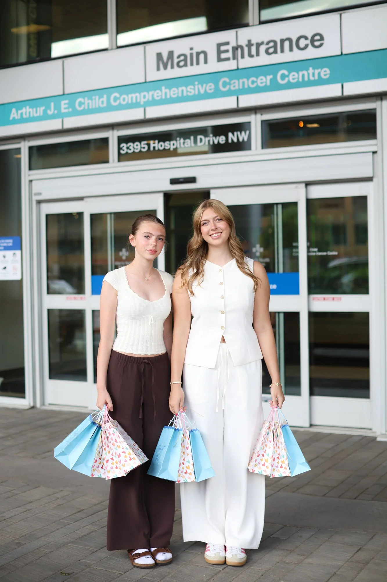 Two women standing outside the Arthur J. E. Child Comprehensive Cancer Centre main entrance, holding shopping bags and smiling.