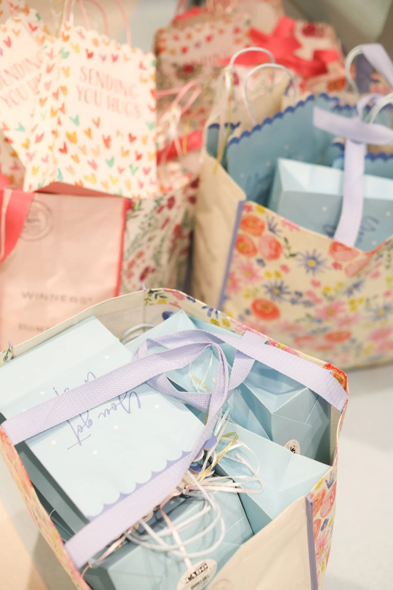 Multiple decorative gift bags with pastel and floral designs, containing presents and tissue paper.