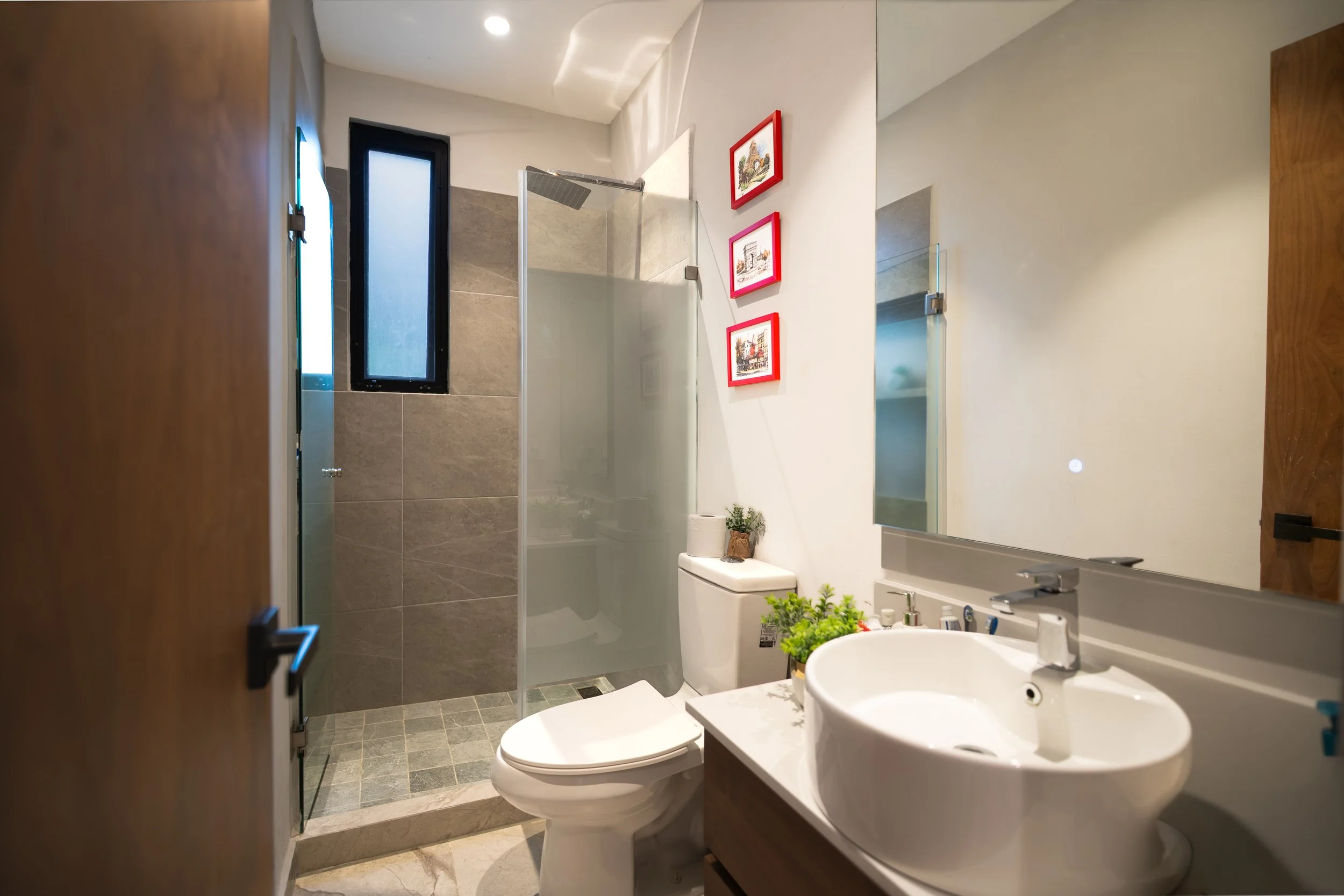 Modern bathroom with walk-in glass shower, toilet, vessel sink, large mirror, and framed artwork