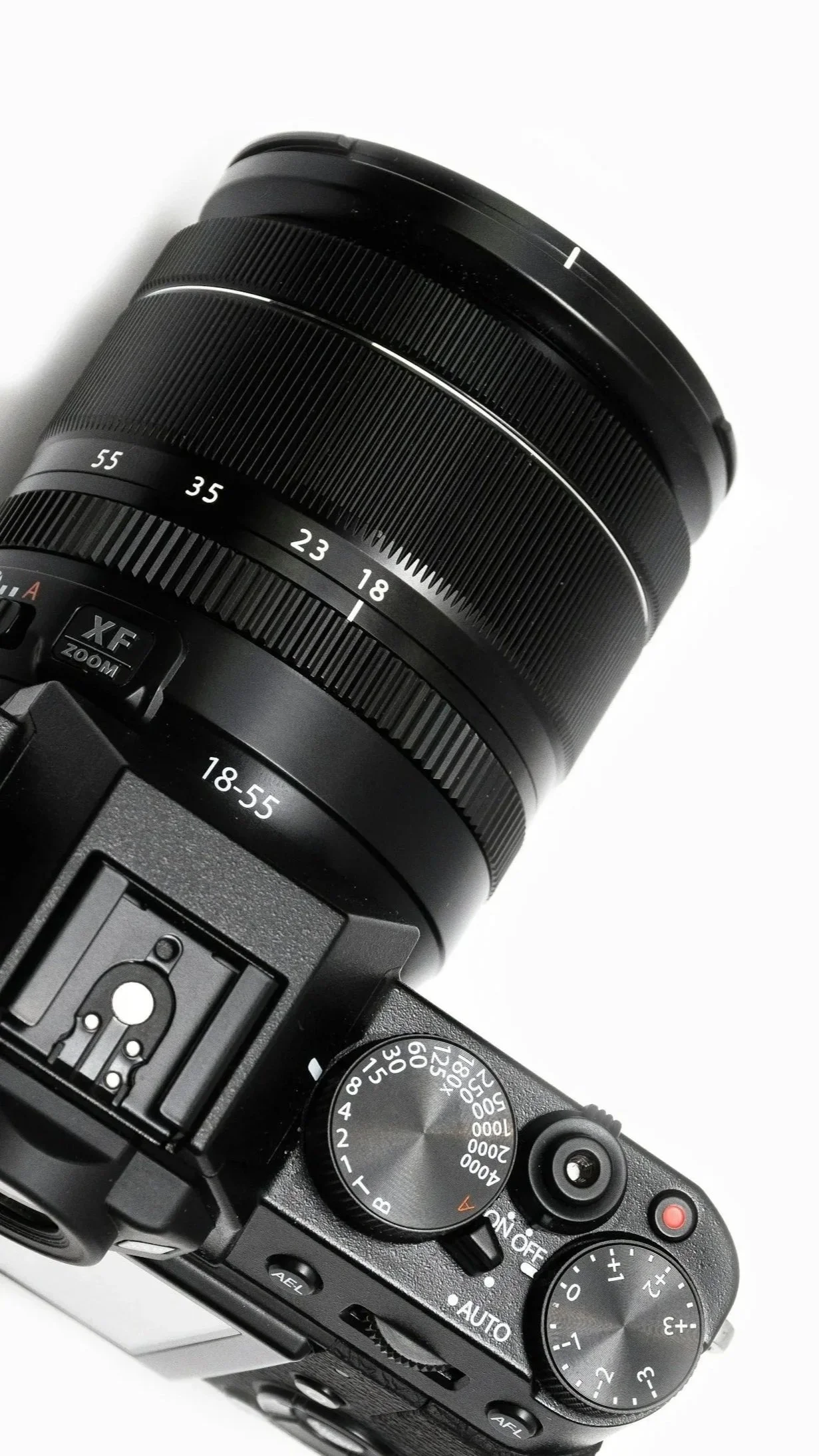 Close-up of a professional black digital camera with a zoom lens marked from 18-55mm, showing top controls including shutter speed dial, ISO dial, and various buttons.