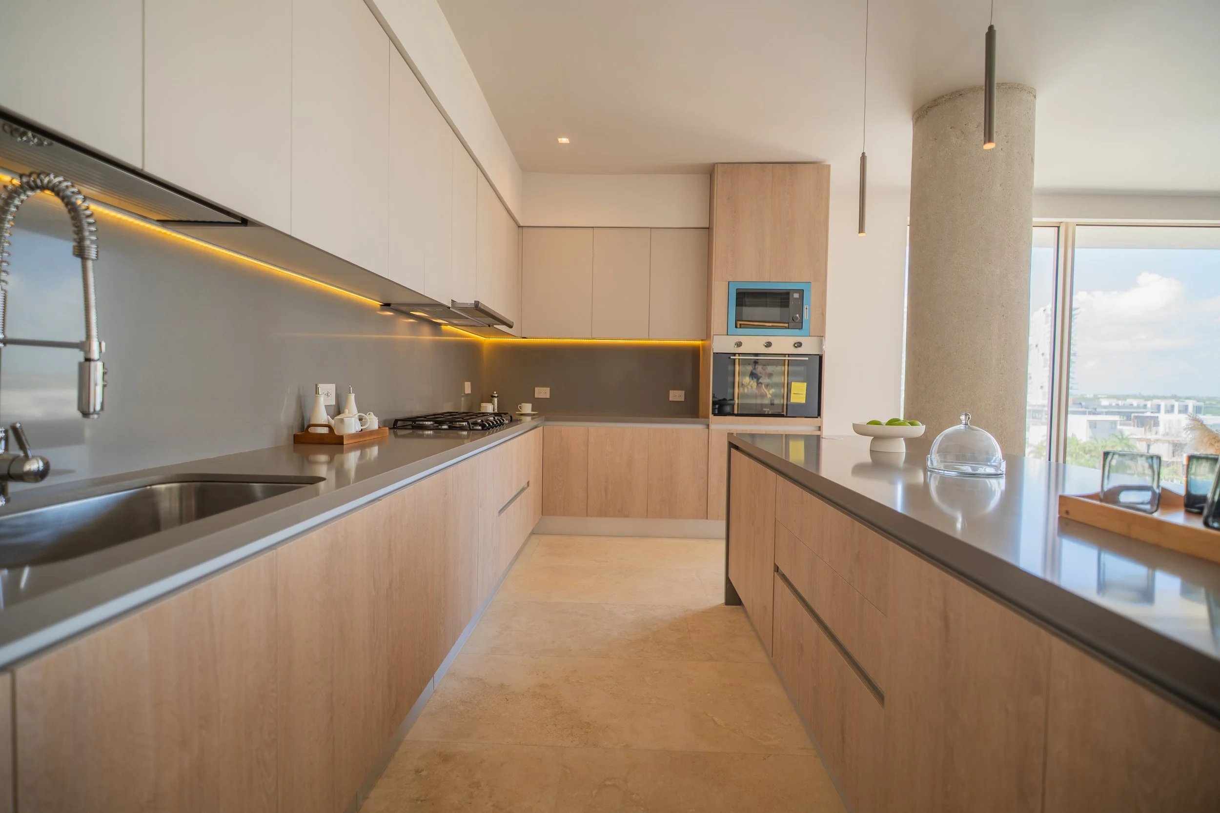 Modern open-concept kitchen with light wood cabinets, stainless-steel sink, gas cooktop, built-in oven, island, and city-view windows