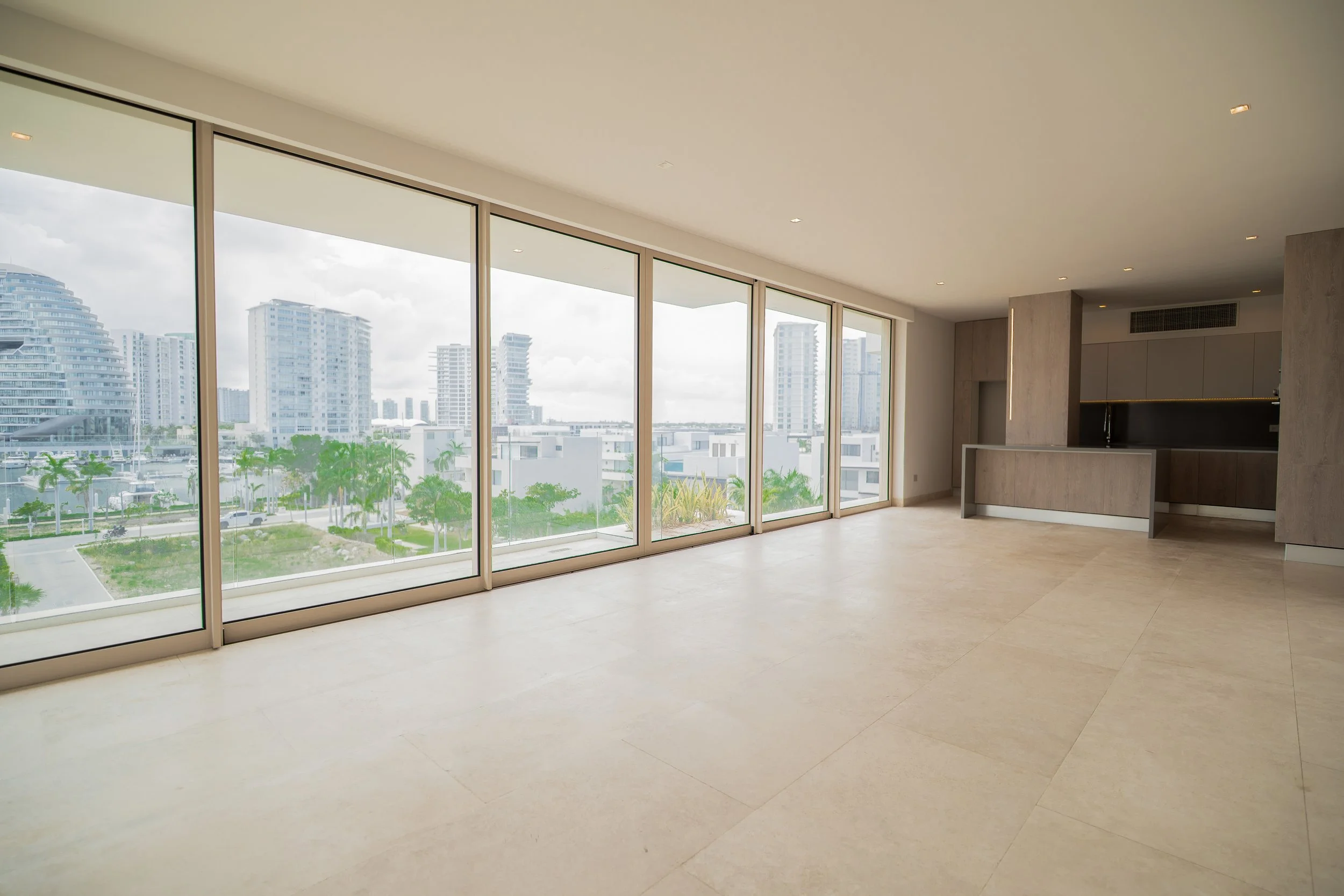 Modern luxury apartment interior with floor-to-ceiling windows, city skyline, palm trees, and a sleek kitchen island