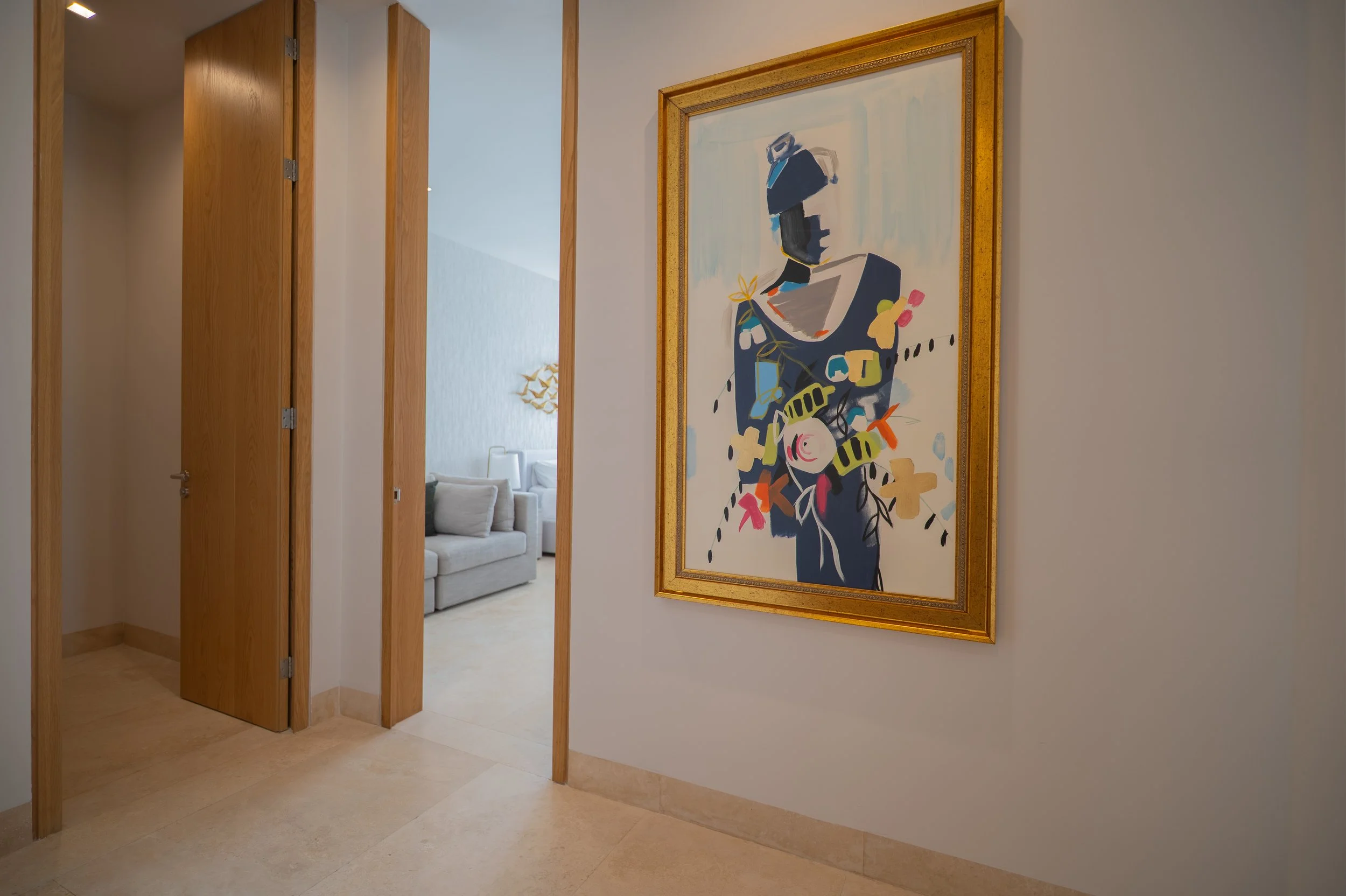 Hallway with open wooden doors, beige tile flooring, and a large colorful abstract painting in a gold frame.