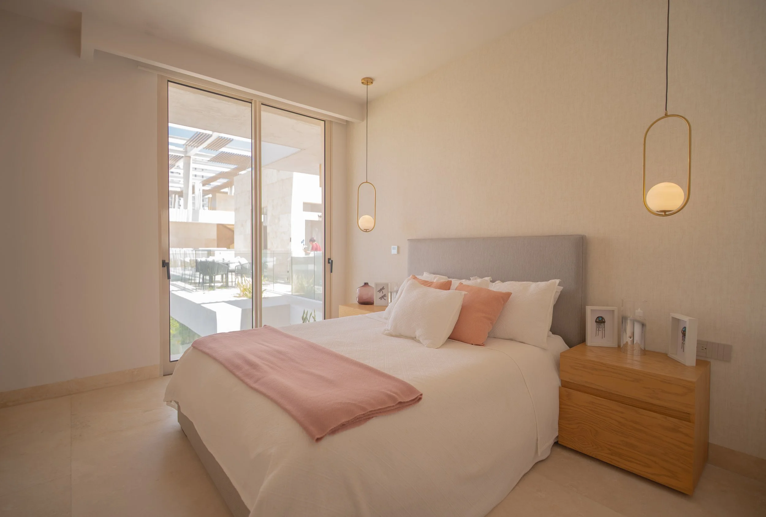 Modern bedroom with a white bed, pink throw blanket, pendant lights, wooden nightstand, and patio view