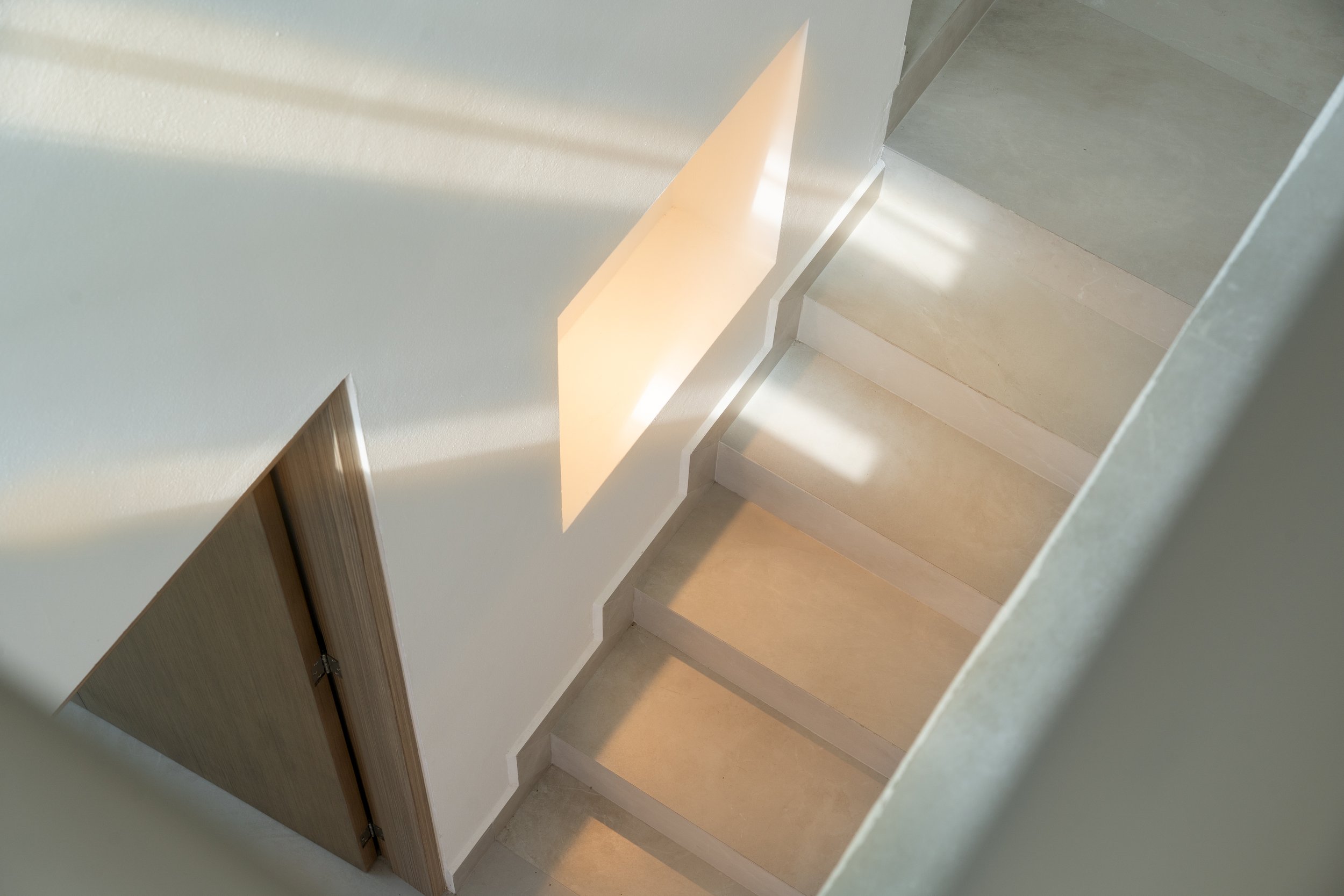 Interior view of a staircase with steps and a wall, illuminated by sunlight.