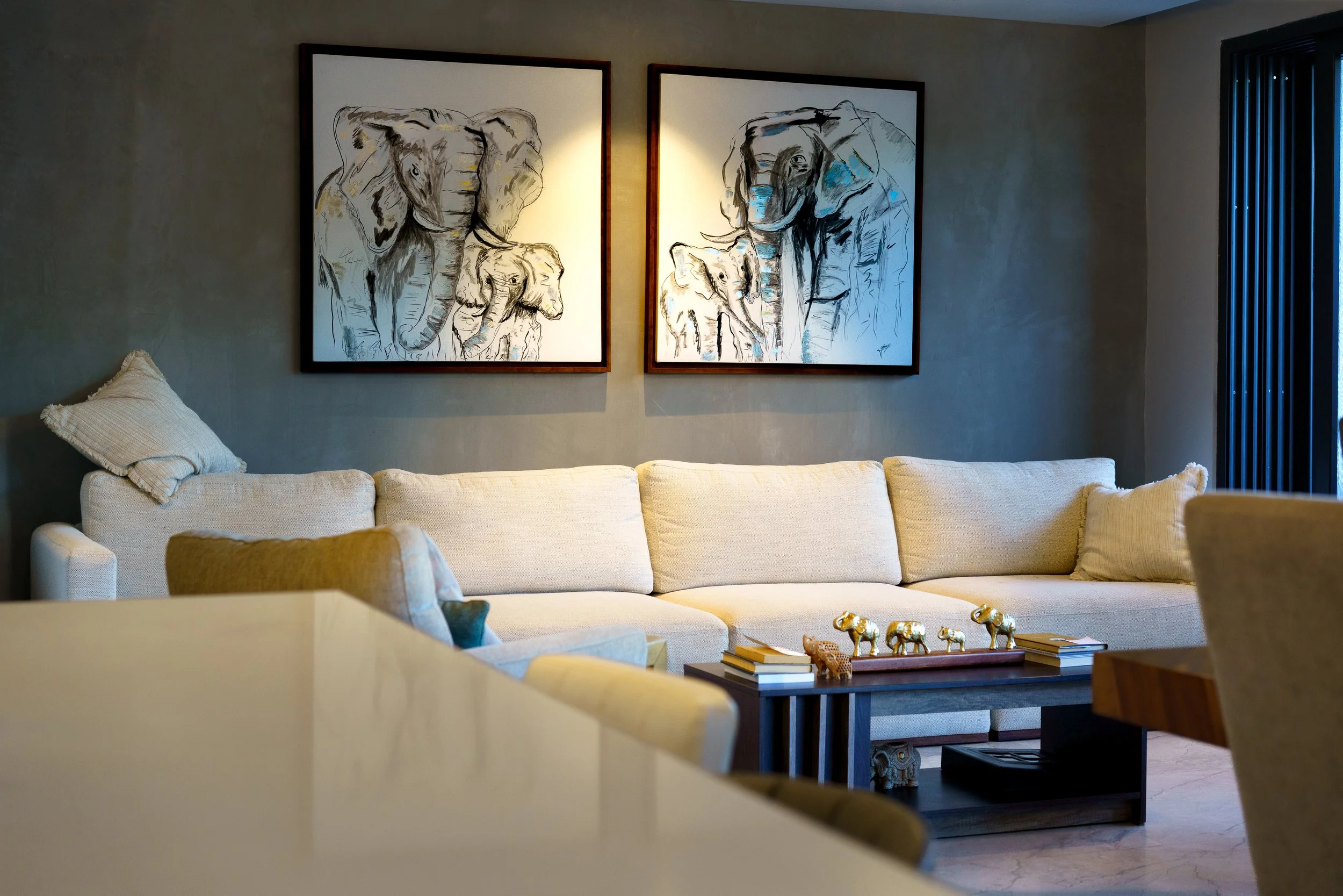 Modern living room with a cream sectional sofa, elephant artwork, and elephant figurines on a coffee table