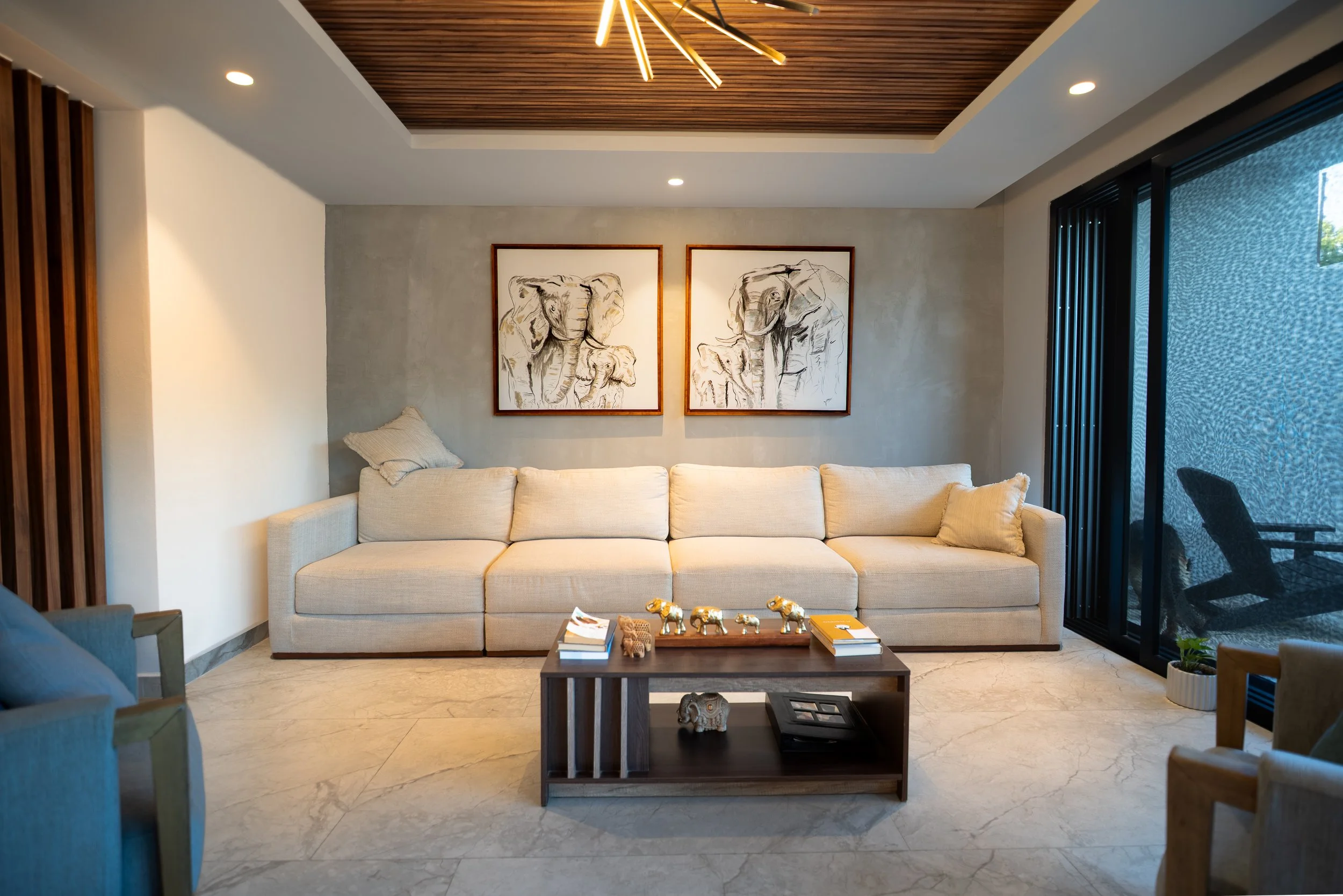 Modern living room with a beige sectional sofa, elephant artwork, wooden coffee table, and contemporary lighting