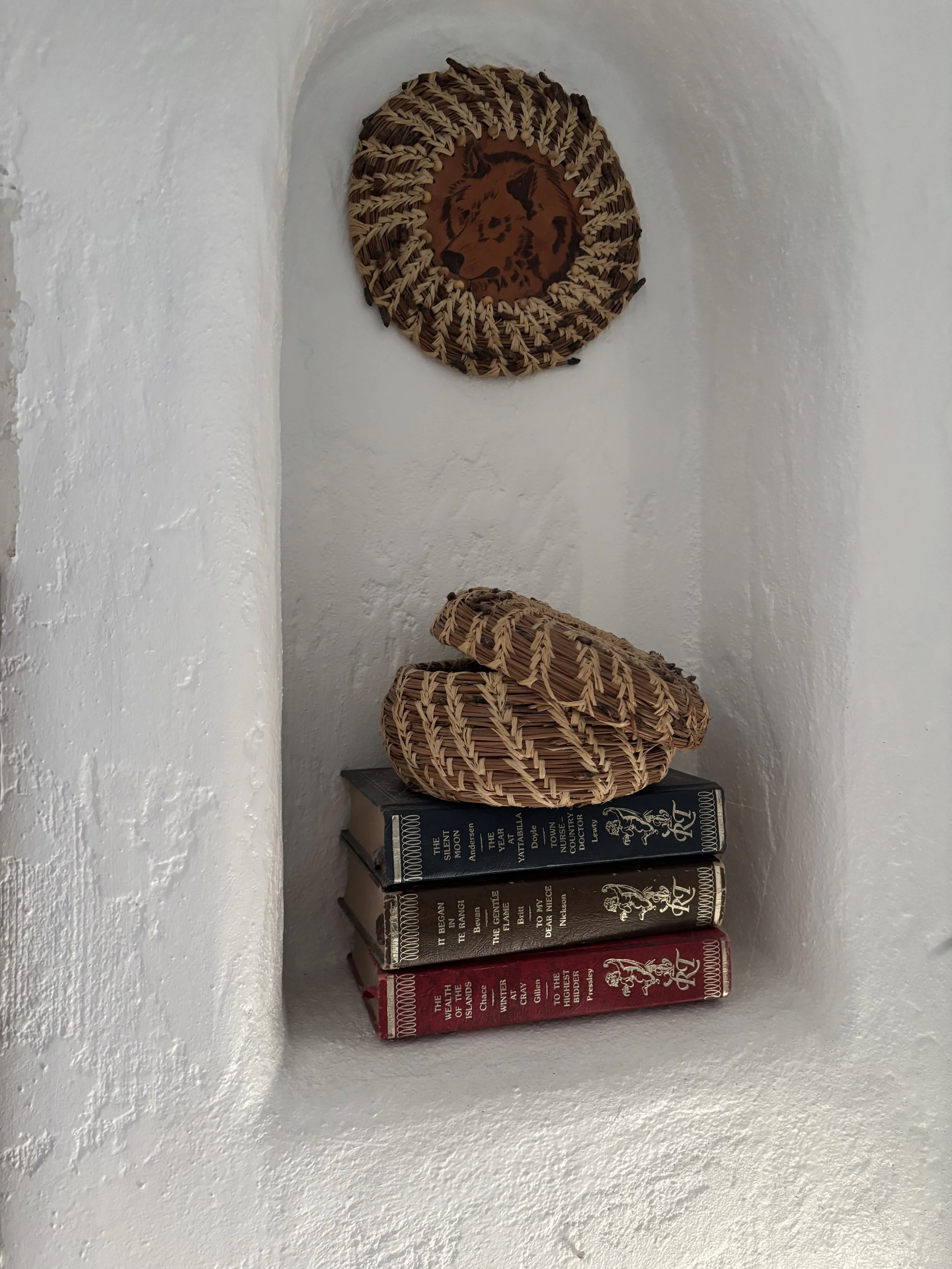 Wicker basket with lion drawing on the inside, resting on top of a stack of vintage books, set against a white textured wall.