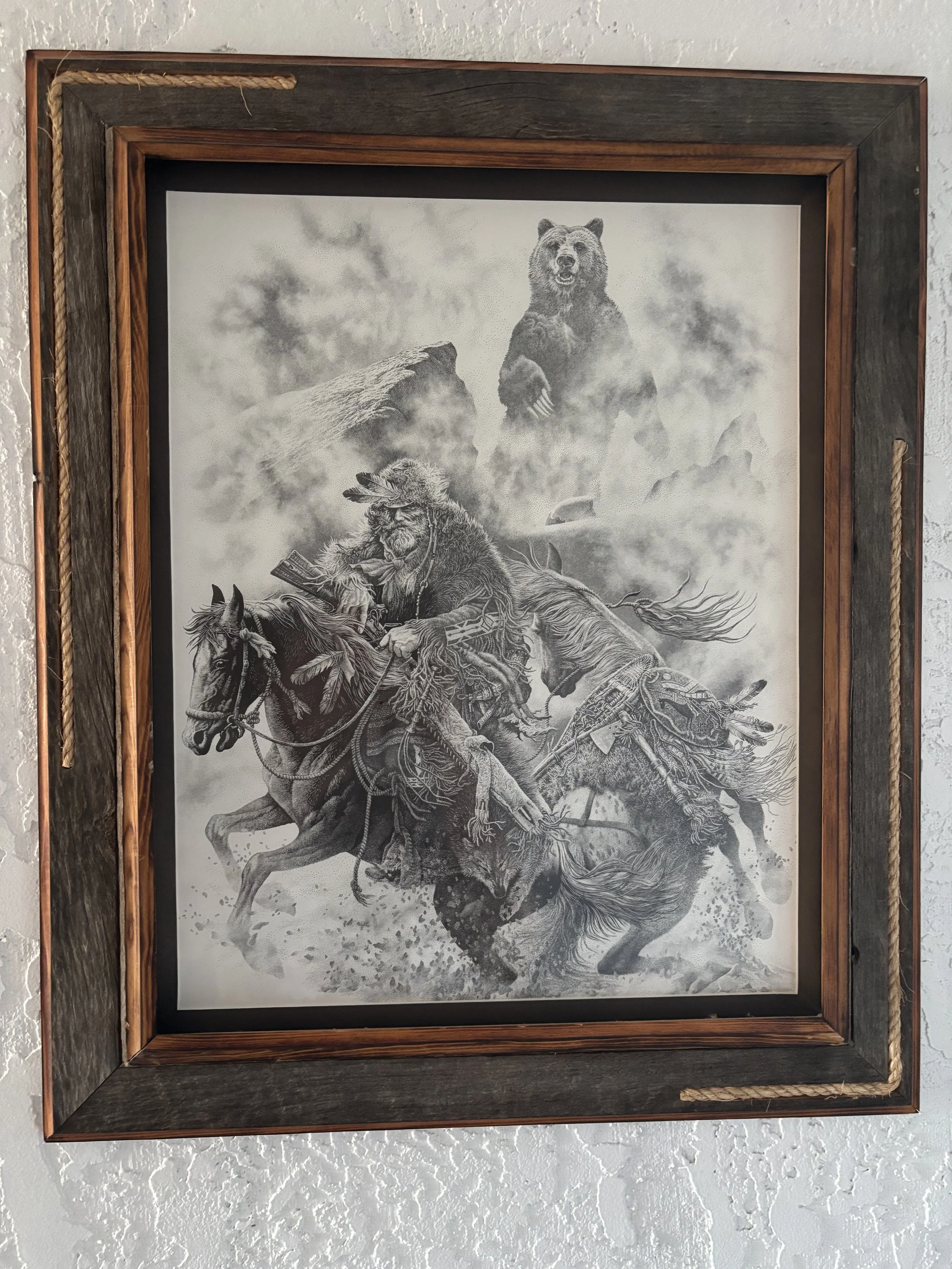 A framed black and white drawing of a Native American chief riding a horse, with a bear standing on a rocky ledge in the background and clouds in the sky.