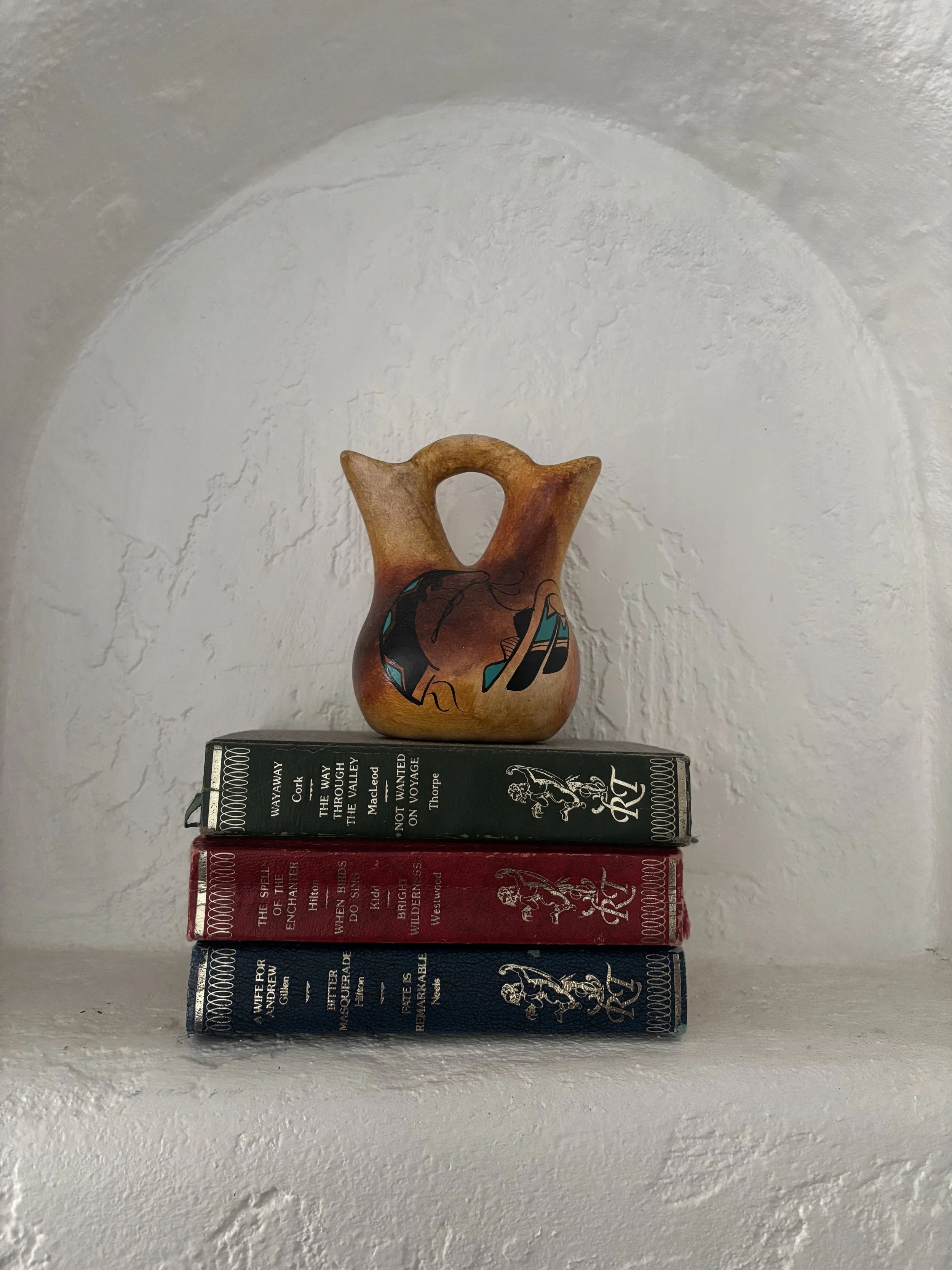 Stack of four vintage hardcover books with a decorative vase on top, placed against a textured white wall.