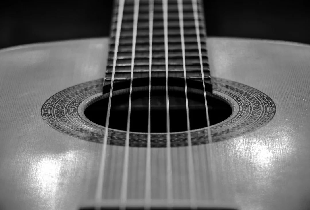 Close-up of a classical guitar's sound hole and strings in black and white.