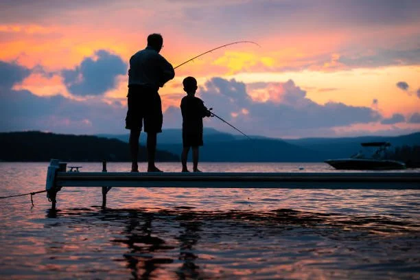 A Father and son fishing off a dock on a lake during sunset