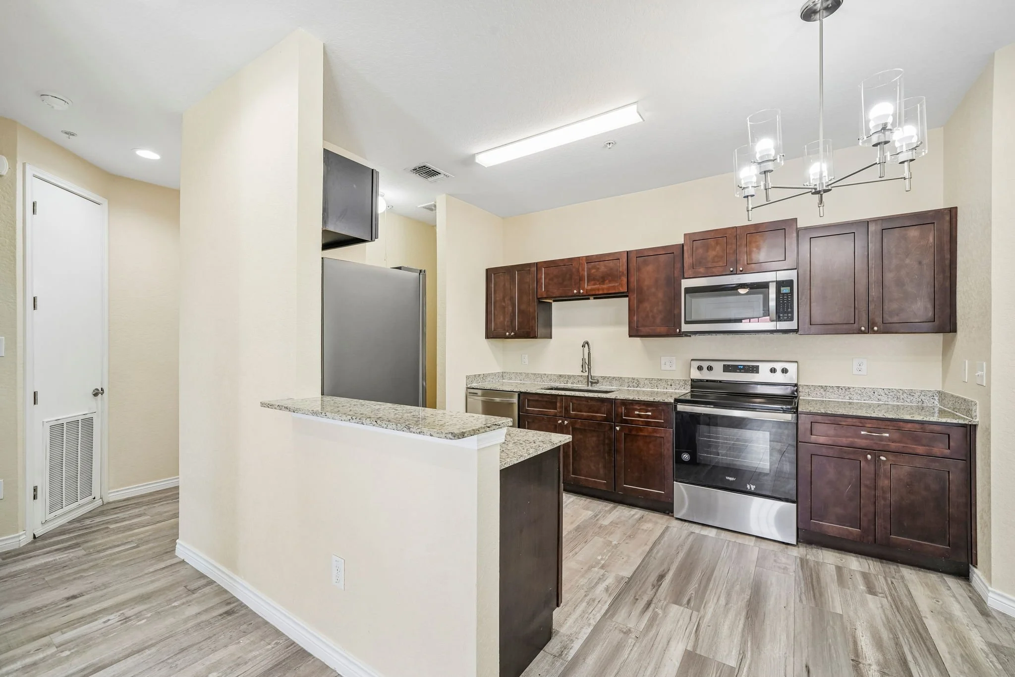 Modern kitchen with dark wood cabinets, stainless steel appliances, granite countertops, and a chandelier with multiple glass shades.