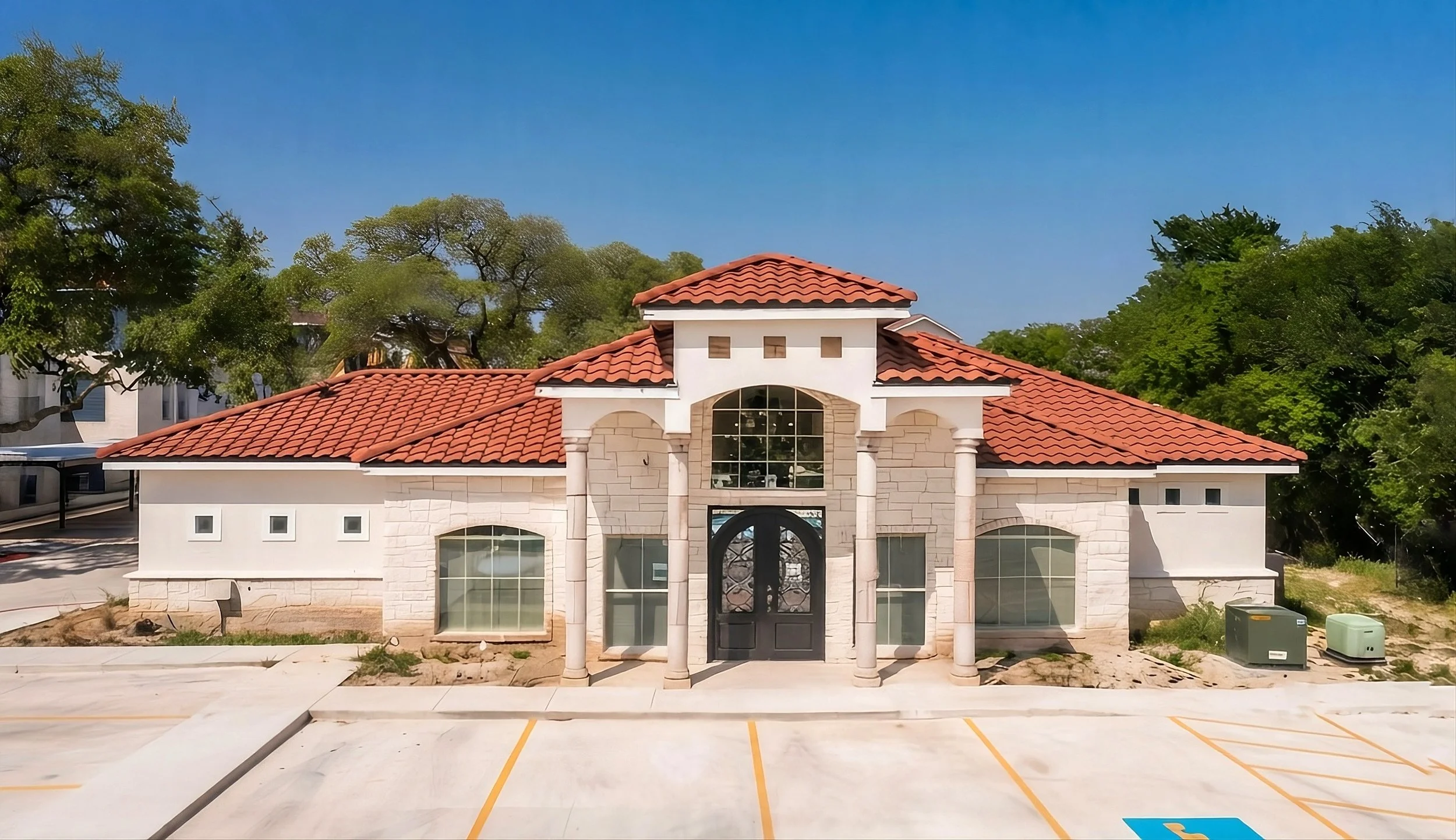 The beautifully designed clubhouse at La Marquesa Apartments with white stone walls and a red tiled roof, large arched windows, and a front door with a curved glass panel, located in San Antonio, Texas.