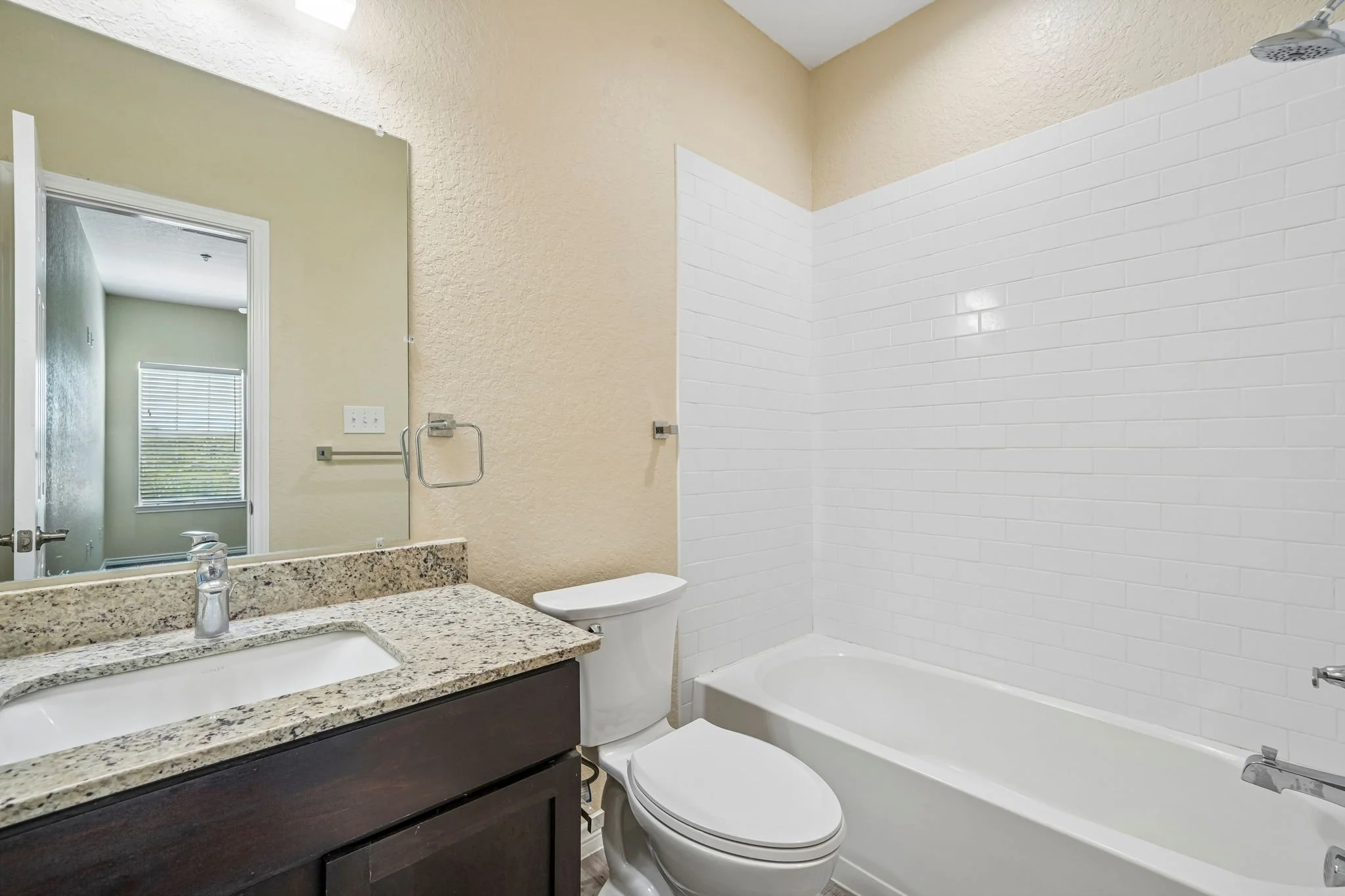 Bathroom with a granite countertop vanity, a mirror, a toilet, and a bathtub with white subway tile walls and a showerhead.