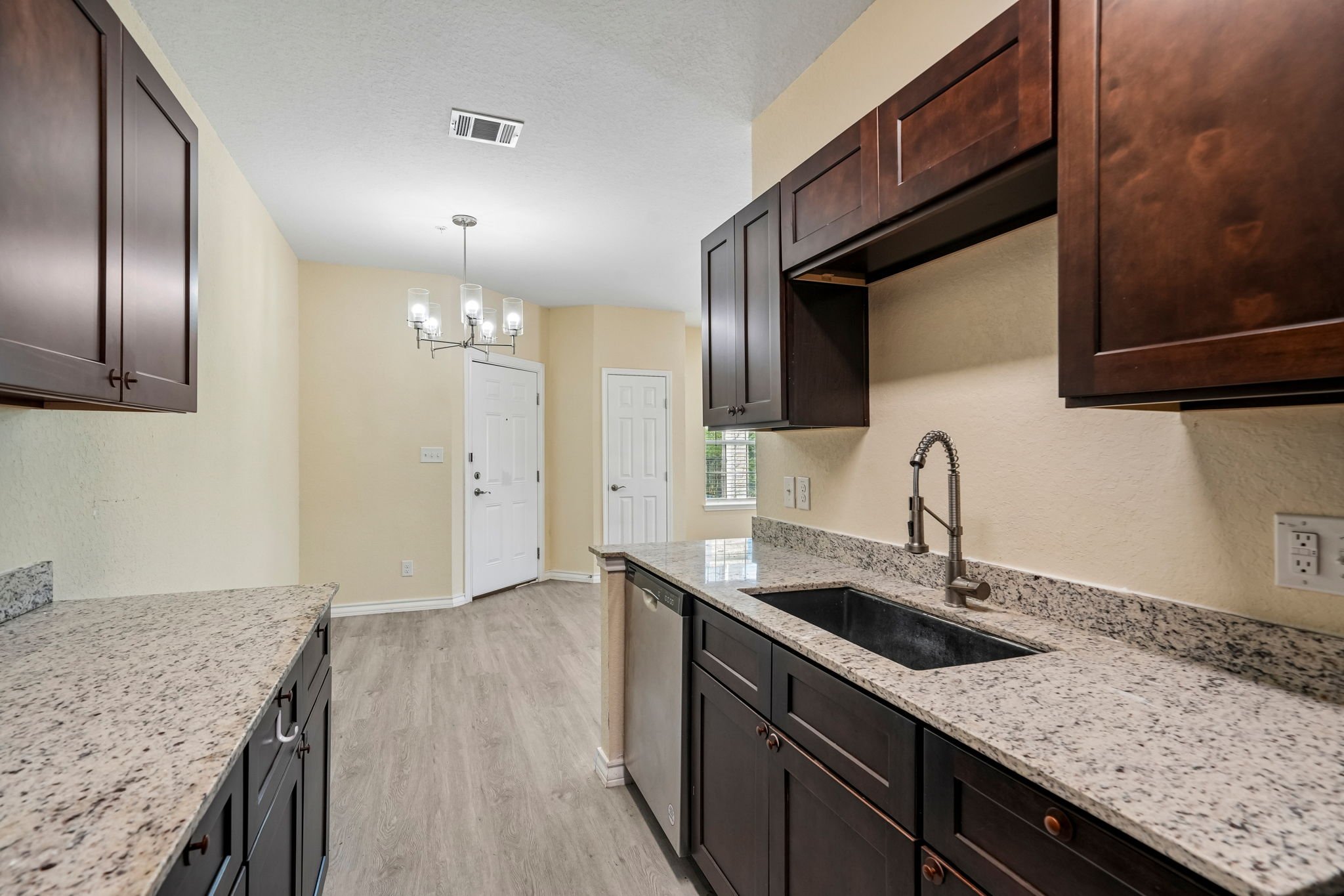 Kitchen with dark wood cabinets, granite countertops, stainless steel faucet, light-colored walls, and a chandelier in the dining area.