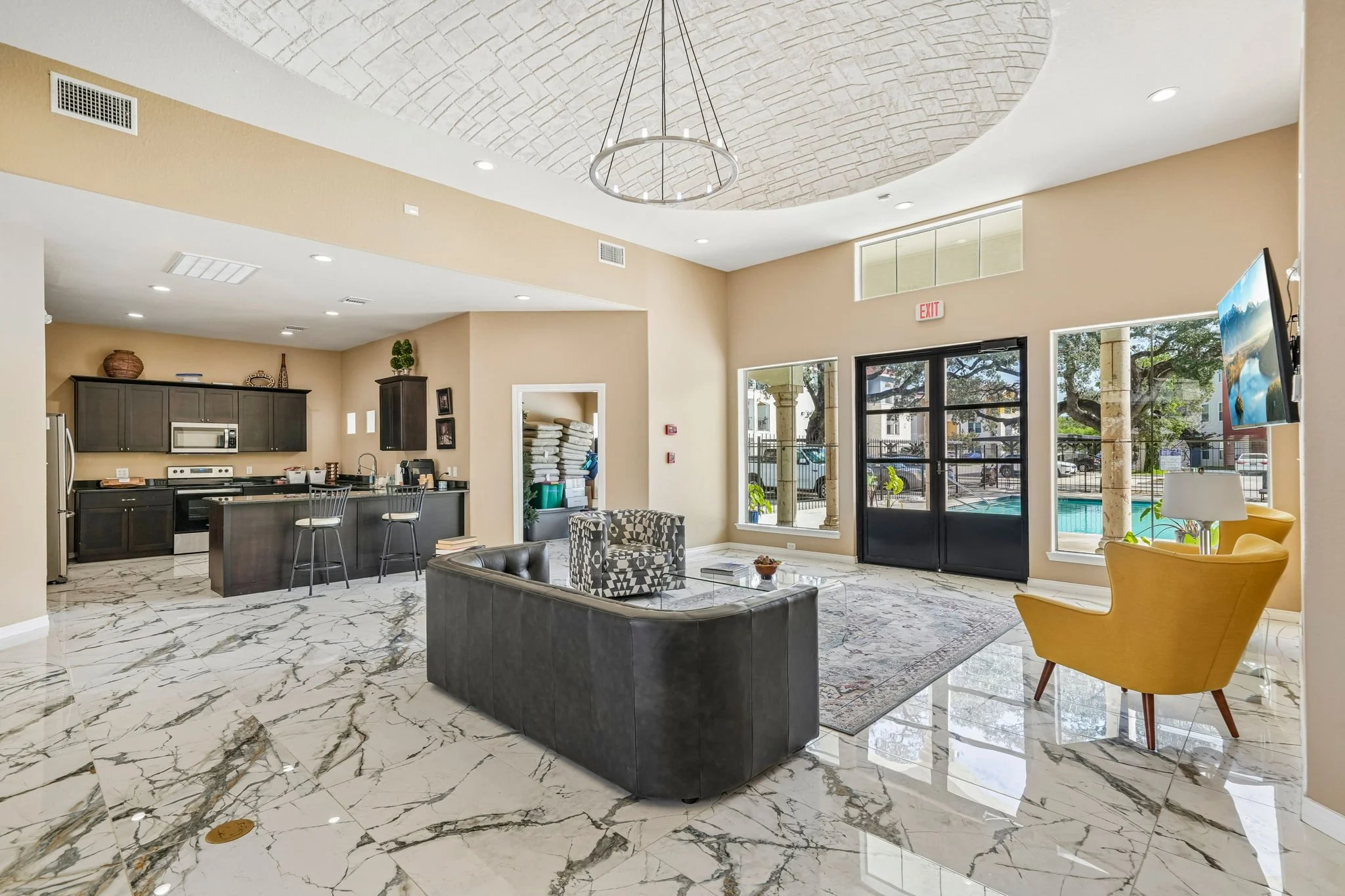 Interior of the La Marquesa clubhouse with marble flooring, large windows, a ceiling with an arch design, a circular hanging light fixture, a kitchen with dark cabinets and stainless steel appliances, and a sitting area.