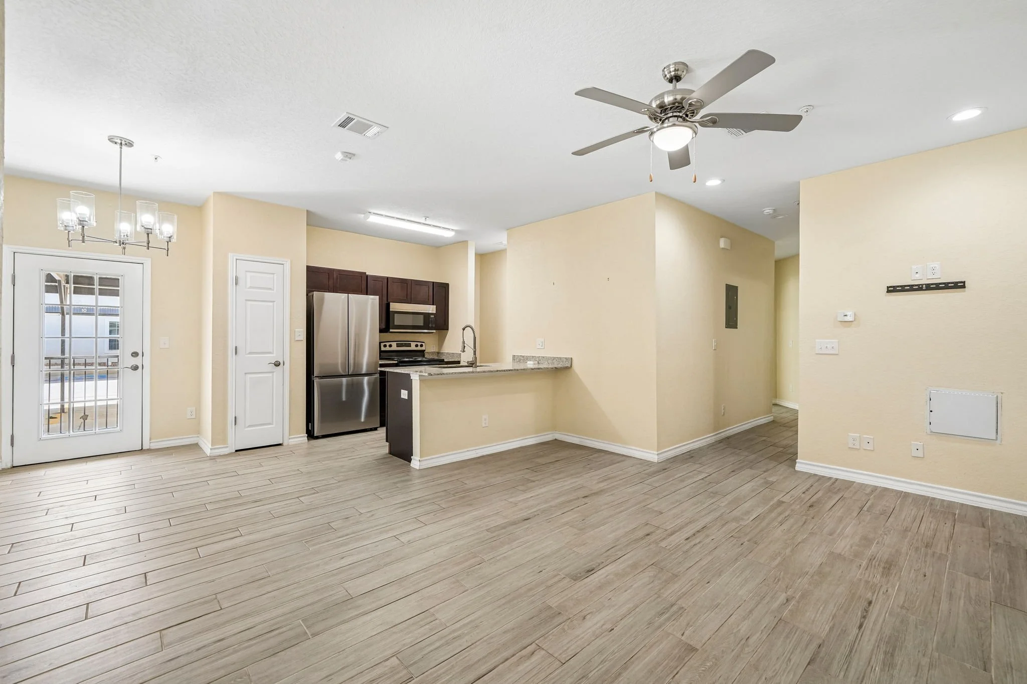 Empty open-concept kitchen and living area with wood-look flooring, a ceiling fan, and a dining area with a chandelier.