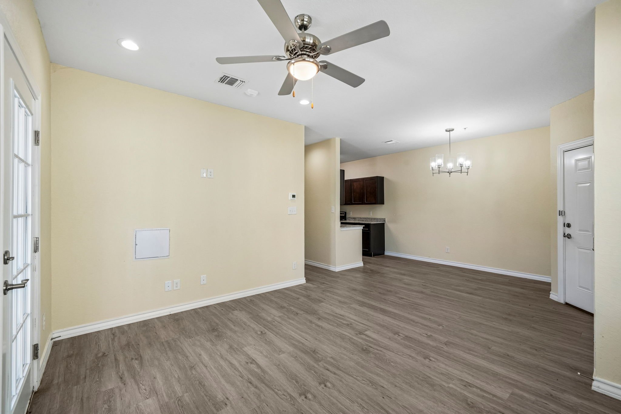 Empty living room with light-colored walls, wood flooring, ceiling fan, and modern lighting fixtures.