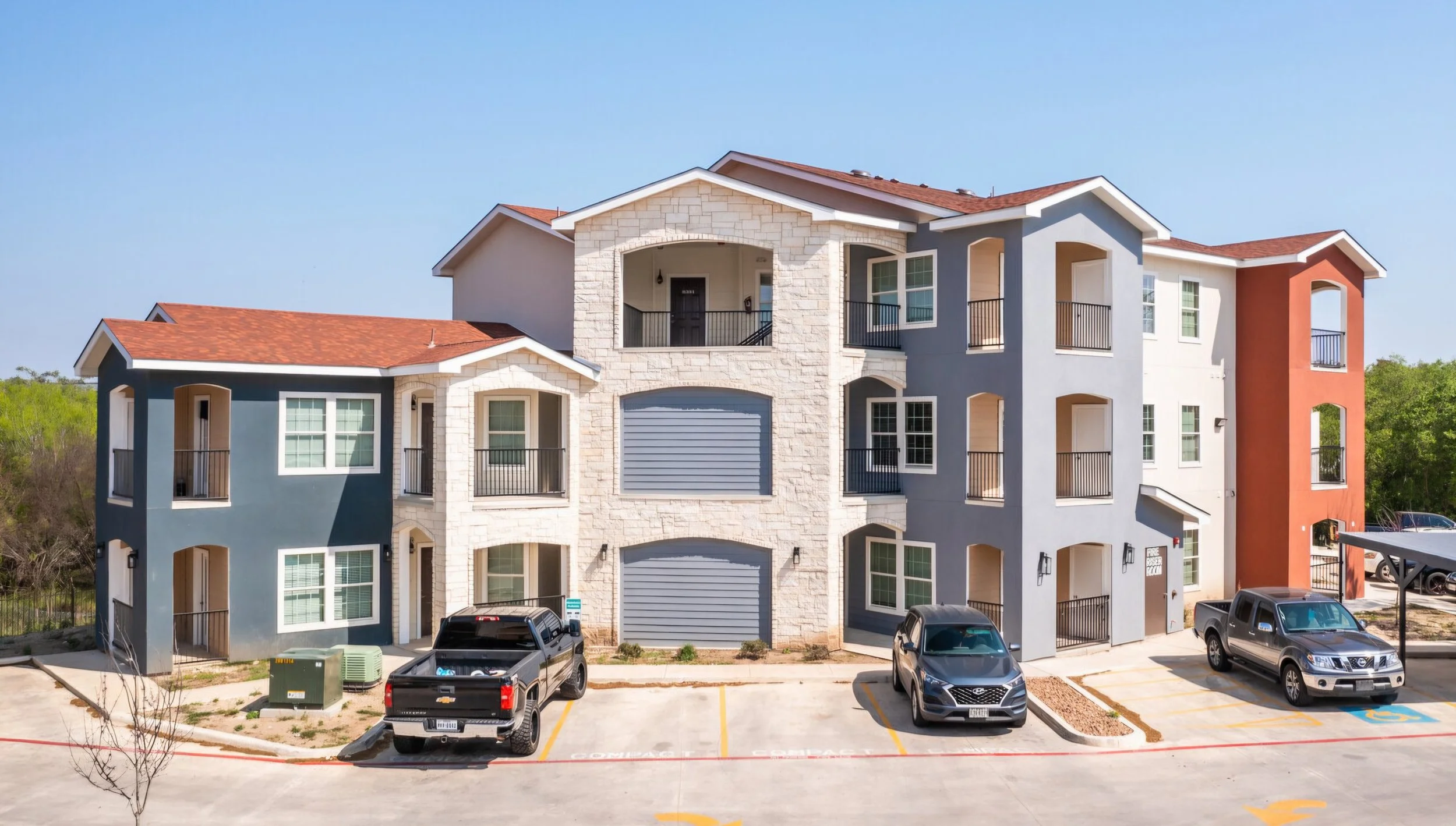 Exterior of a residential building at La Marquesa Apartments with blue, white, beige, and orange exterior walls, balconies, and a red tile roof, with parked cars in front.