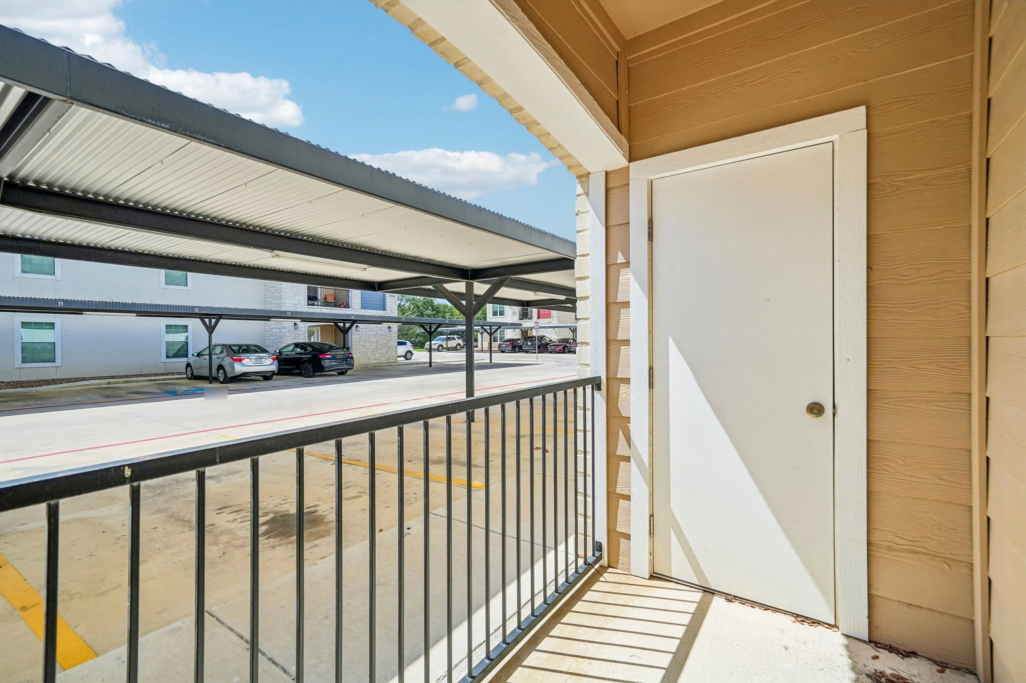 View from a patio at La Marquesa Apartments with black metal railing and a wooden wall with a white door.