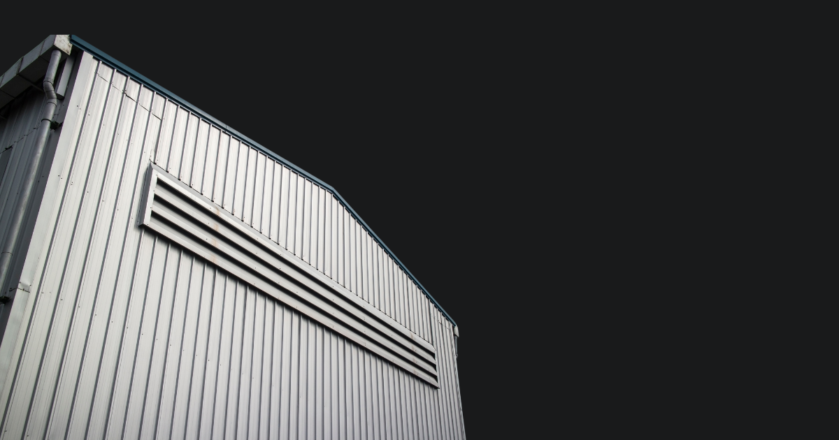 Close-up of a metal building's corner with an air vent, against a dark sky background.
