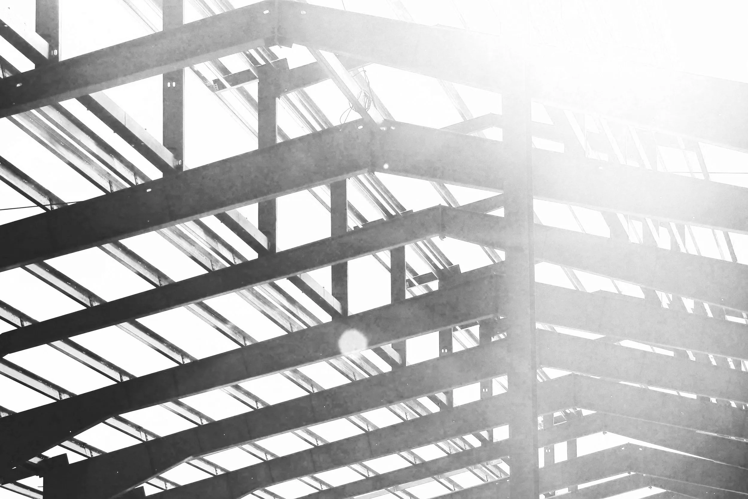 Black and white photo of a multi-level steel and glass staircase inside a building, with sunlight streaming through the glass panels.