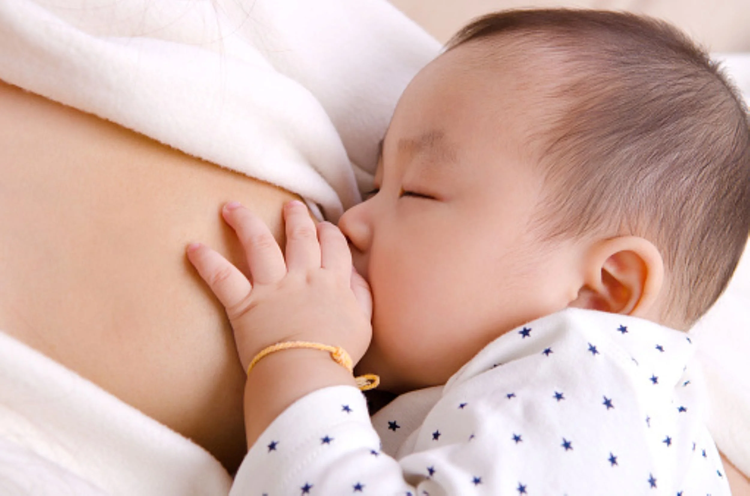 A baby breastfeeding from a mother, with the baby's hand touching the mother's breast.