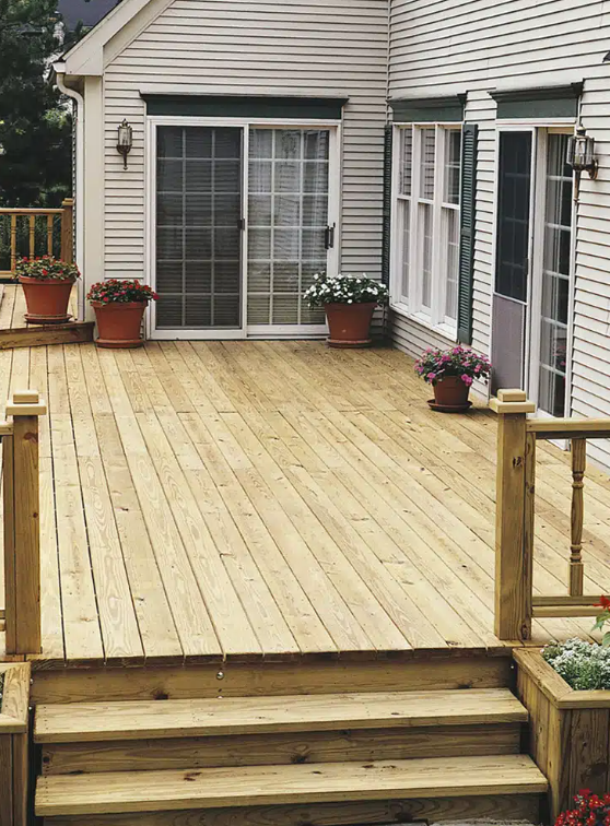 Newly built wooden deck with steps and potted flowers in front of a house with sliding glass doors and windows.