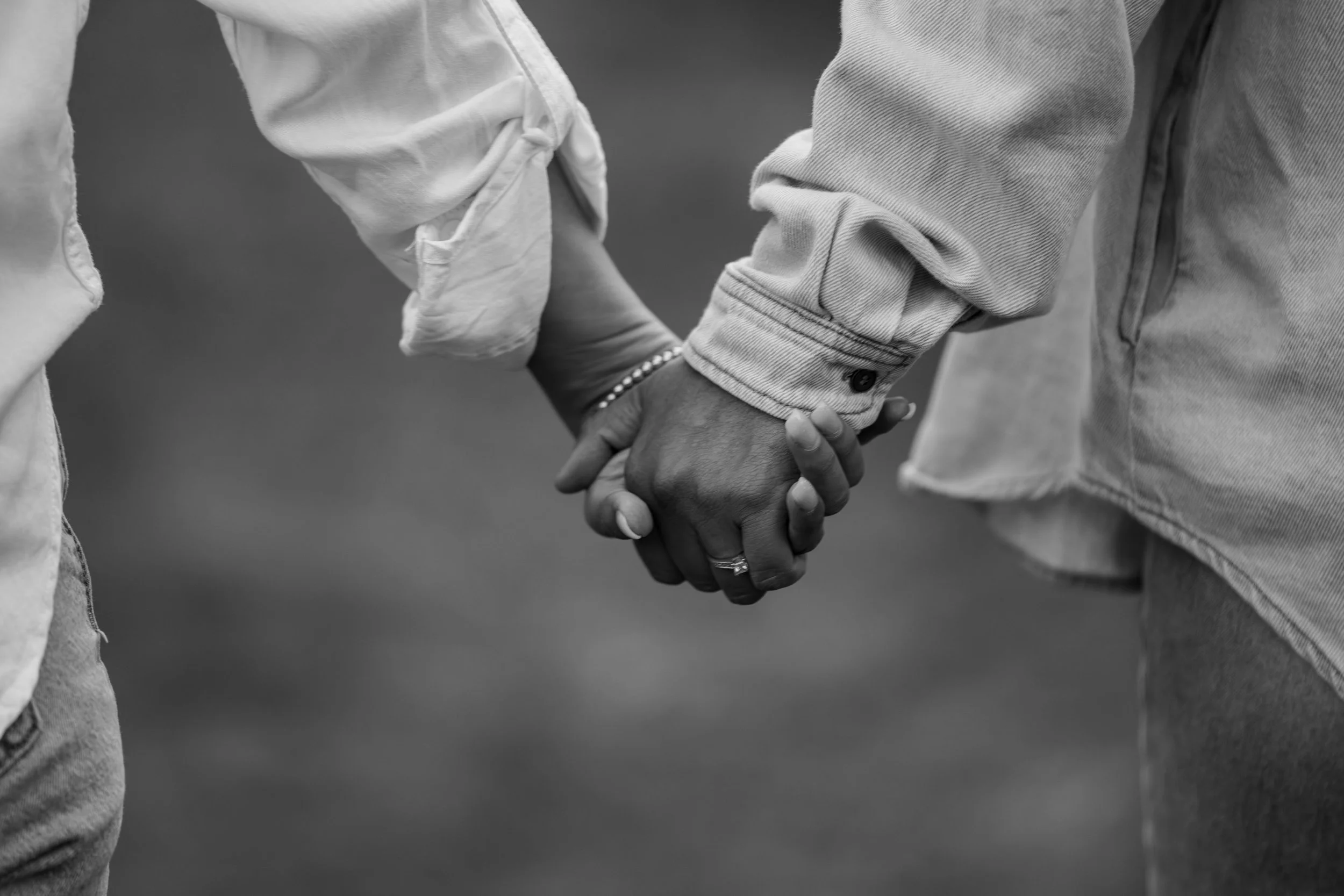 Two people holding hands, one wearing a denim jacket and the other a light-colored shirt, in black and white.