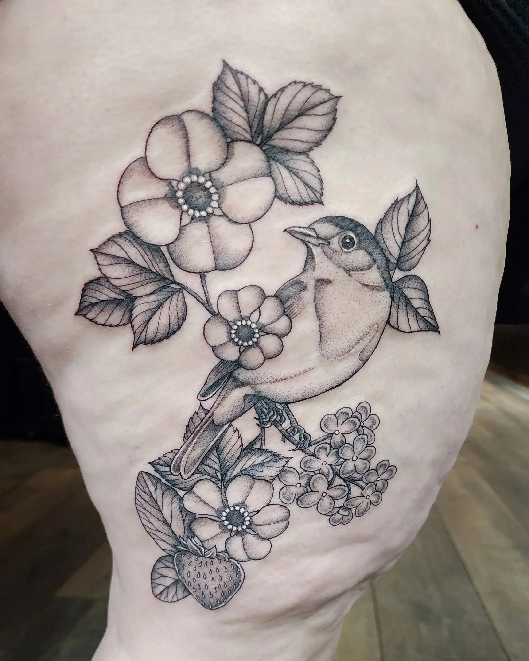 Black and gray tattoo of a bird with flowers and leaves on person's skin.