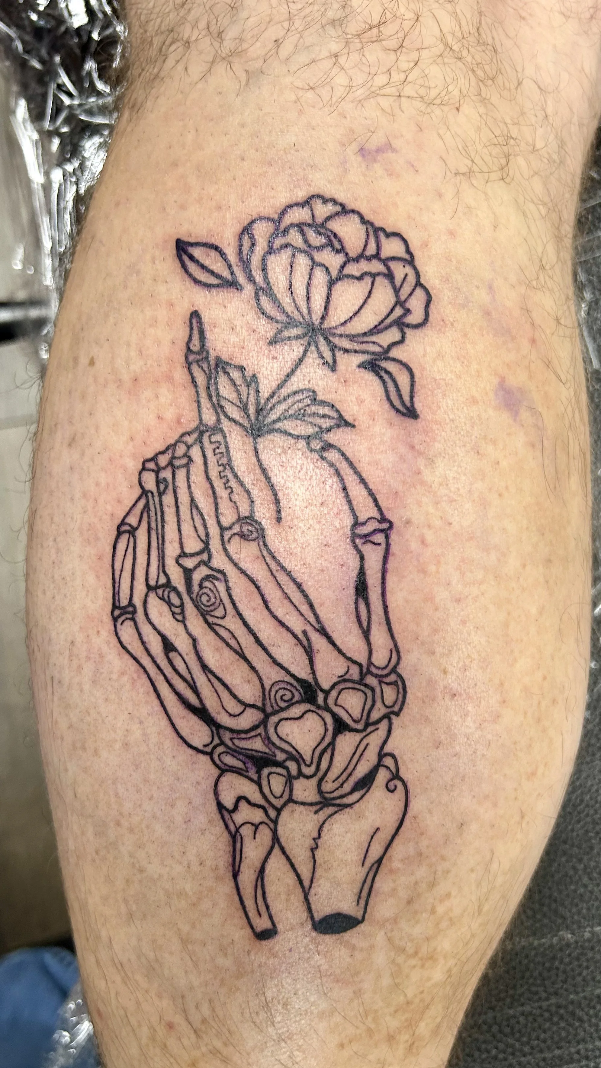 A tattoo of a detailed anatomical skeletal hand holding a blooming flower on a person's arm.