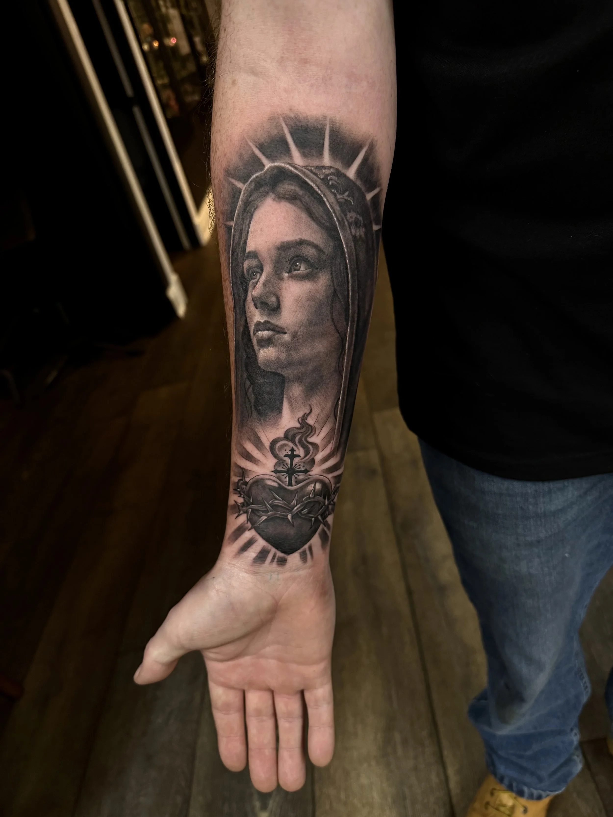 Tattoo of a woman's face, protected by a halo, on a person's forearm.