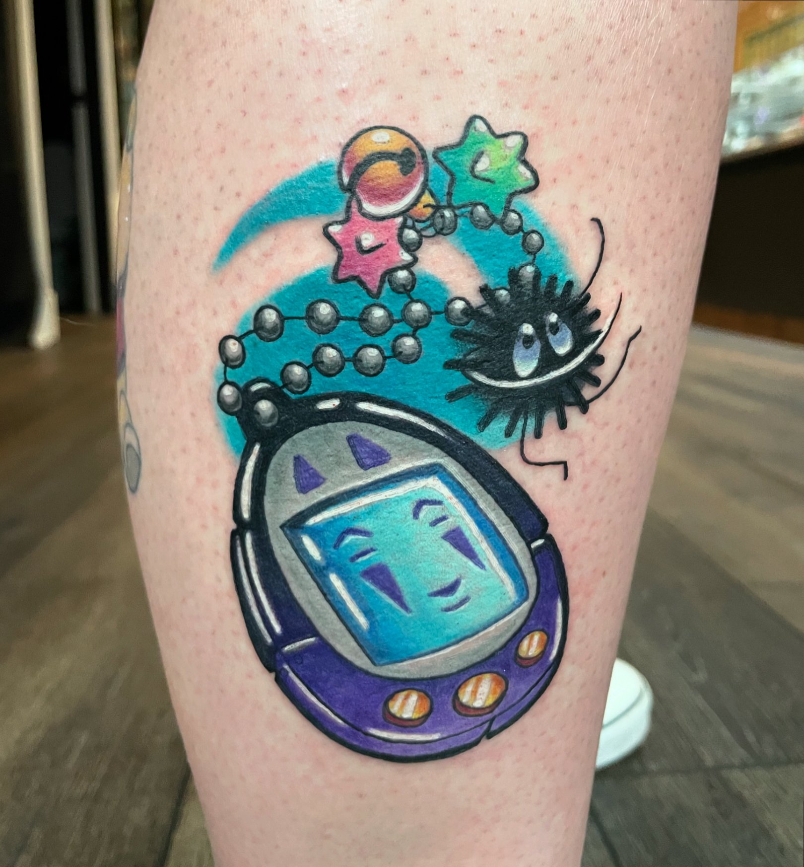 Colorful tattoo of a vintage Game Boy with a chain of cartoon characters and space-themed shapes above it on a person's arm.